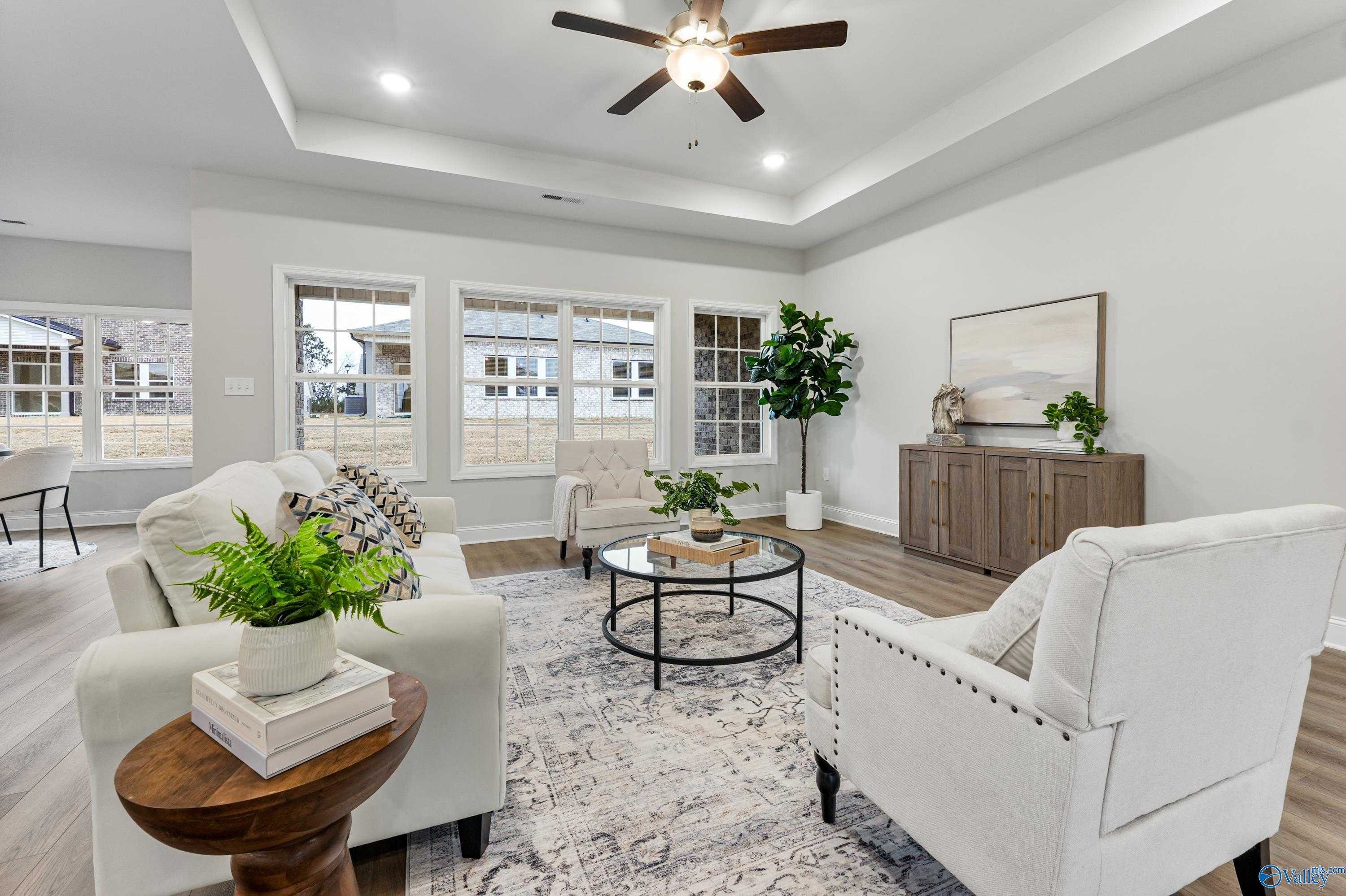 Bright living room with white sofa, armchairs, ceiling fan, plants, and large windows in Davidson Homes The Finleigh, Toney, Alabama