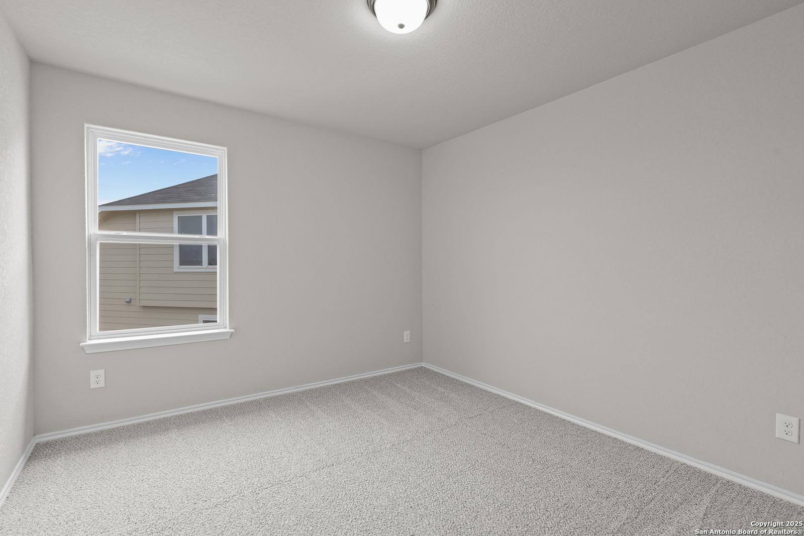 Bright secondary bedroom with neutral gray walls, carpet floor, and window view in Davidson Homes The Murray J, San Antonio
