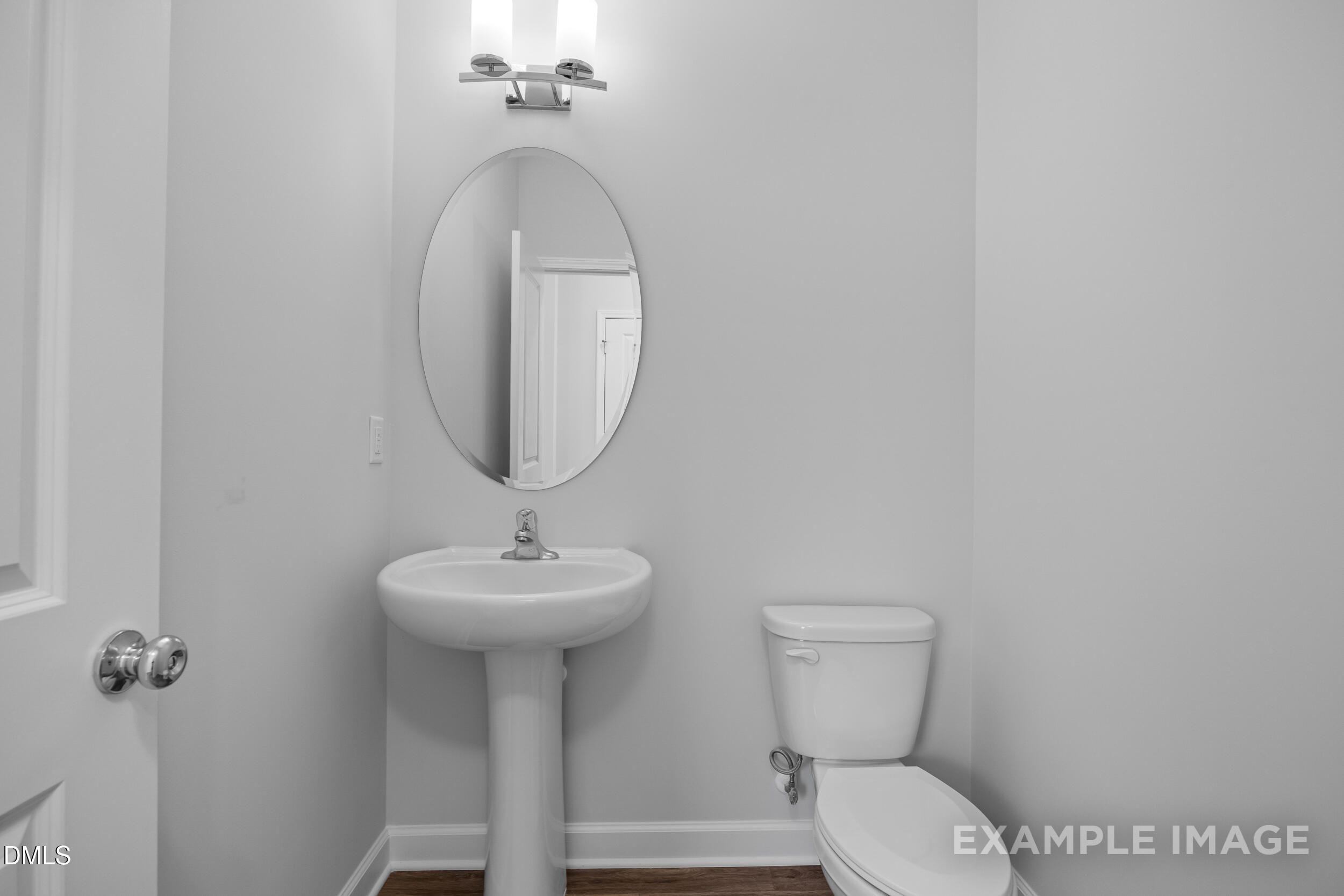 Modern half-bath with pedestal sink, oval mirror, and lighting in The Gavin A home at Gregory Village, Lillington, NC.