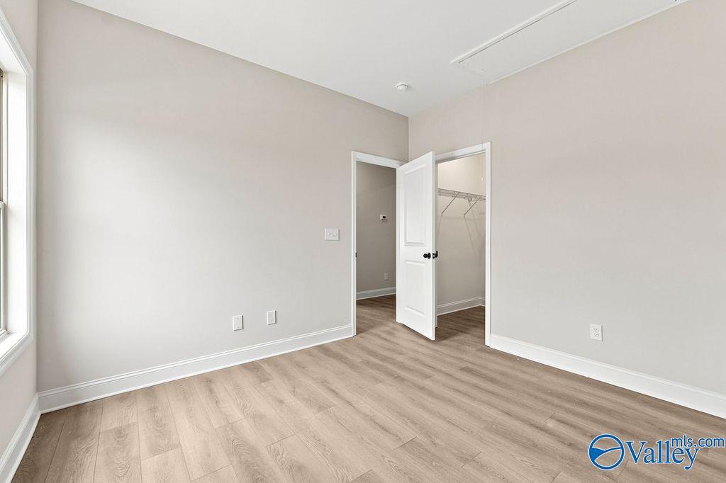 Bright bedroom with neutral walls, wood-look flooring, and walk-in closet in The Camilla B at The Retreat at Cain Park.