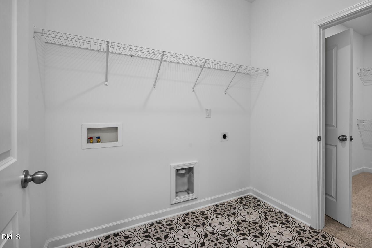 Spacious laundry room featuring wire shelving, utility sink, washer/dryer hookups, and patterned tile floor in Davidson Homes The Cypress B II, Angier, NC