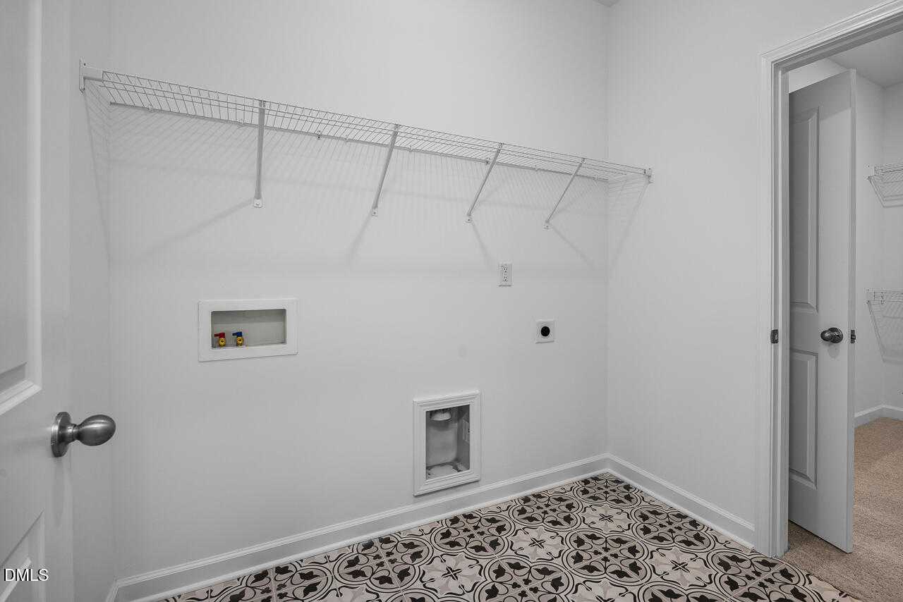 Spacious laundry room featuring wire shelving, utility sink, washer/dryer hookups, and patterned tile floor in Davidson Homes The Cypress B II, Angier, NC