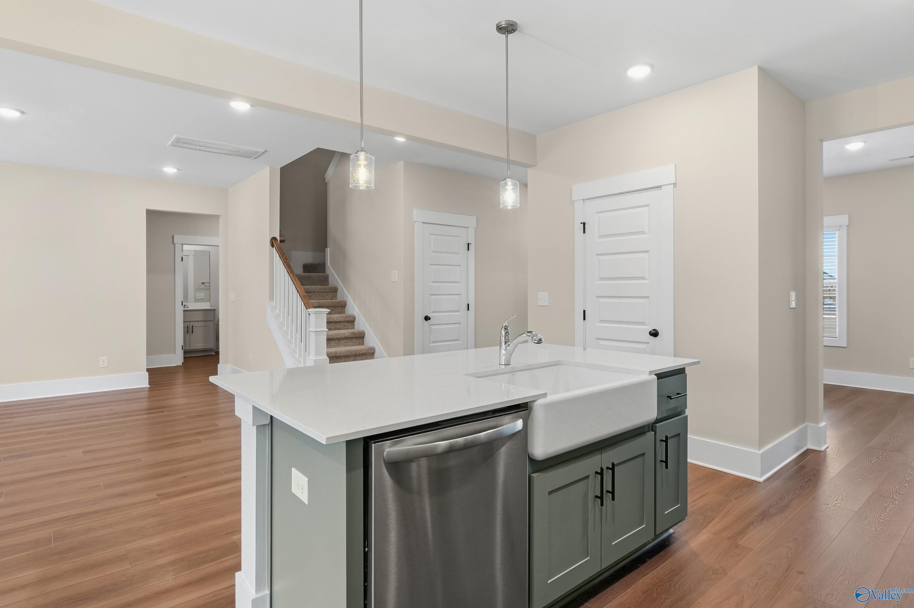 Open-concept kitchen with white quartz island, farmhouse sink, stainless dishwasher, and hardwood floors in Davidson Homes The Shelby A, Athens, Alabama