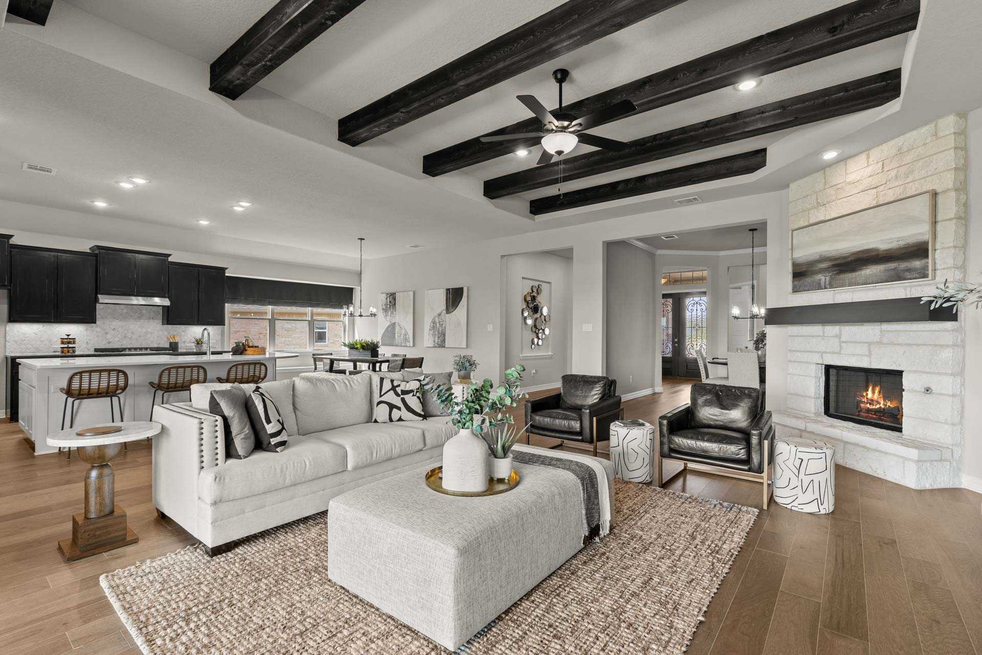 Open-concept living room in The Summerlin B featuring vaulted wooden beams, white sofa, fireplace, and modern kitchen island