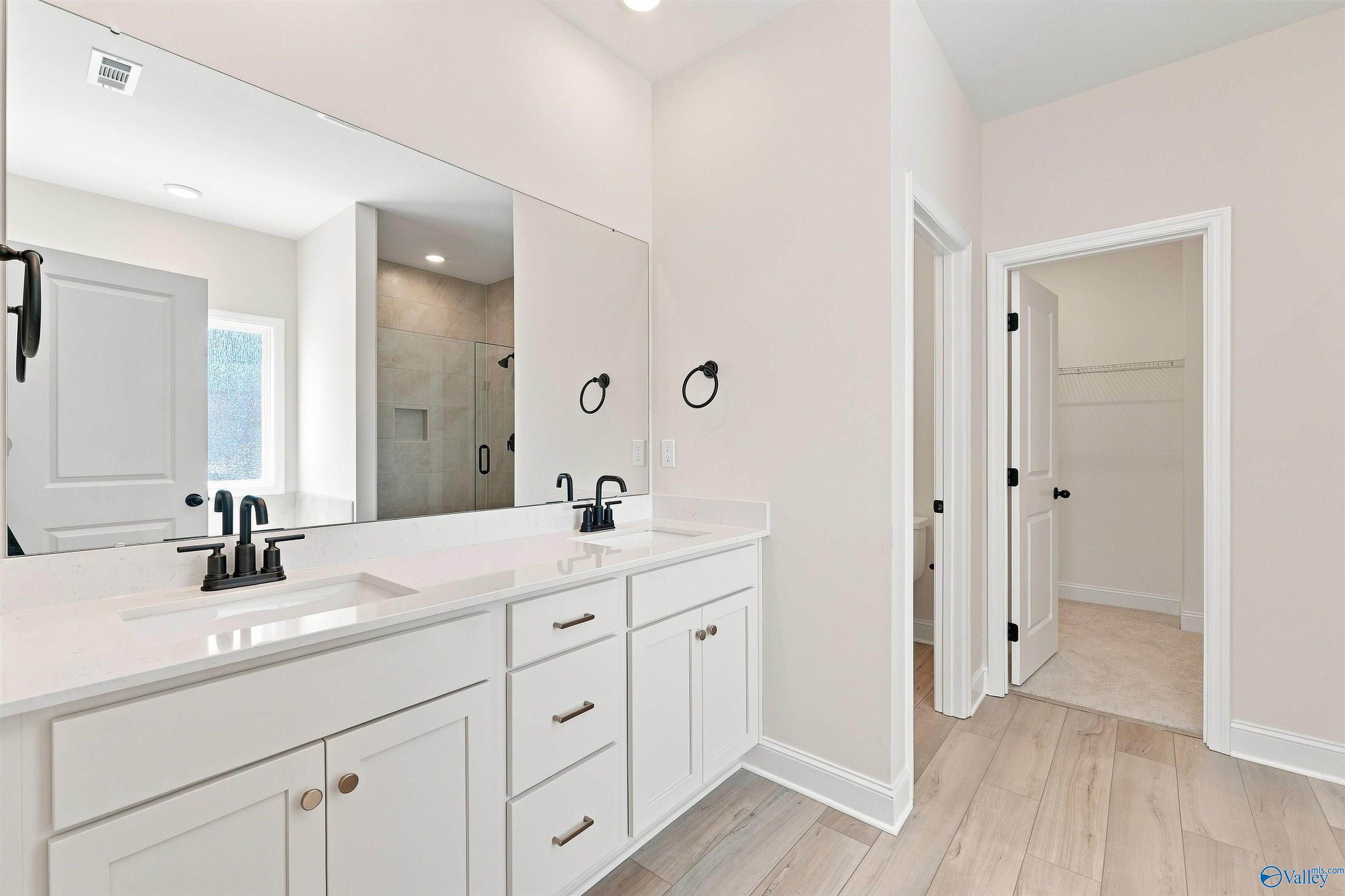 Double vanity bathroom with white cabinetry, matte black faucets, and tile shower in Davidson Homes Everett B plan, Toney, Alabama