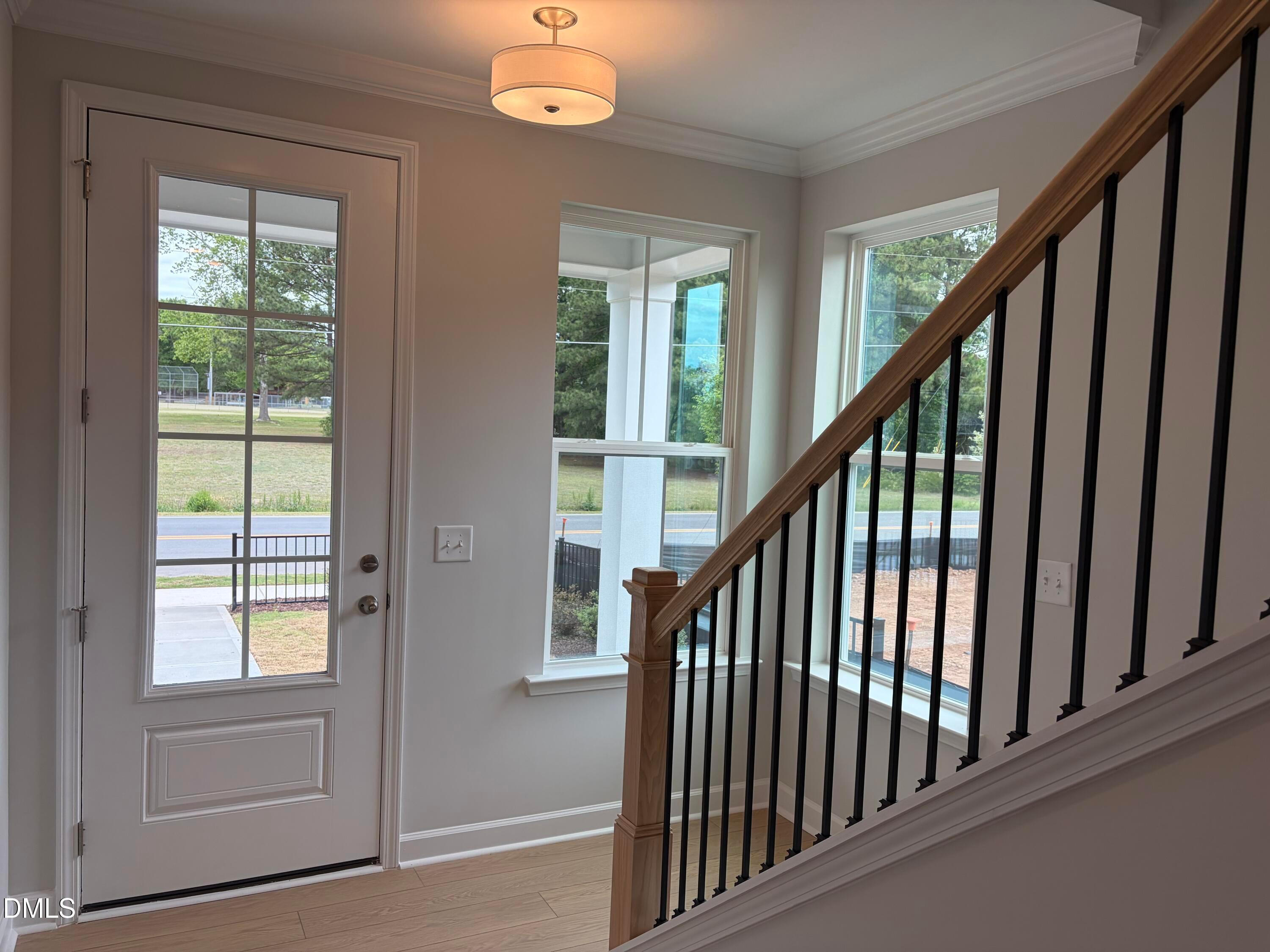 Bright entry foyer with oak staircase, black iron railings, hardwood floors, and exterior views through front door and windows in The Mitchell home, Knightdale, NC