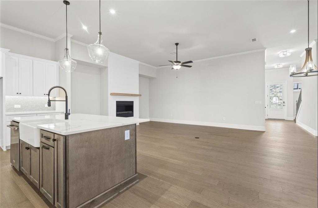 Open-concept great room with white brick gas fireplace, kitchen island sink, hardwood floors in The Seaside A, Woodstock, GA