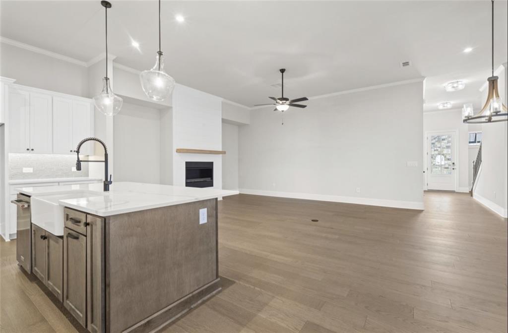 Open-concept great room with white brick gas fireplace, kitchen island sink, hardwood floors in The Seaside A, Woodstock, GA