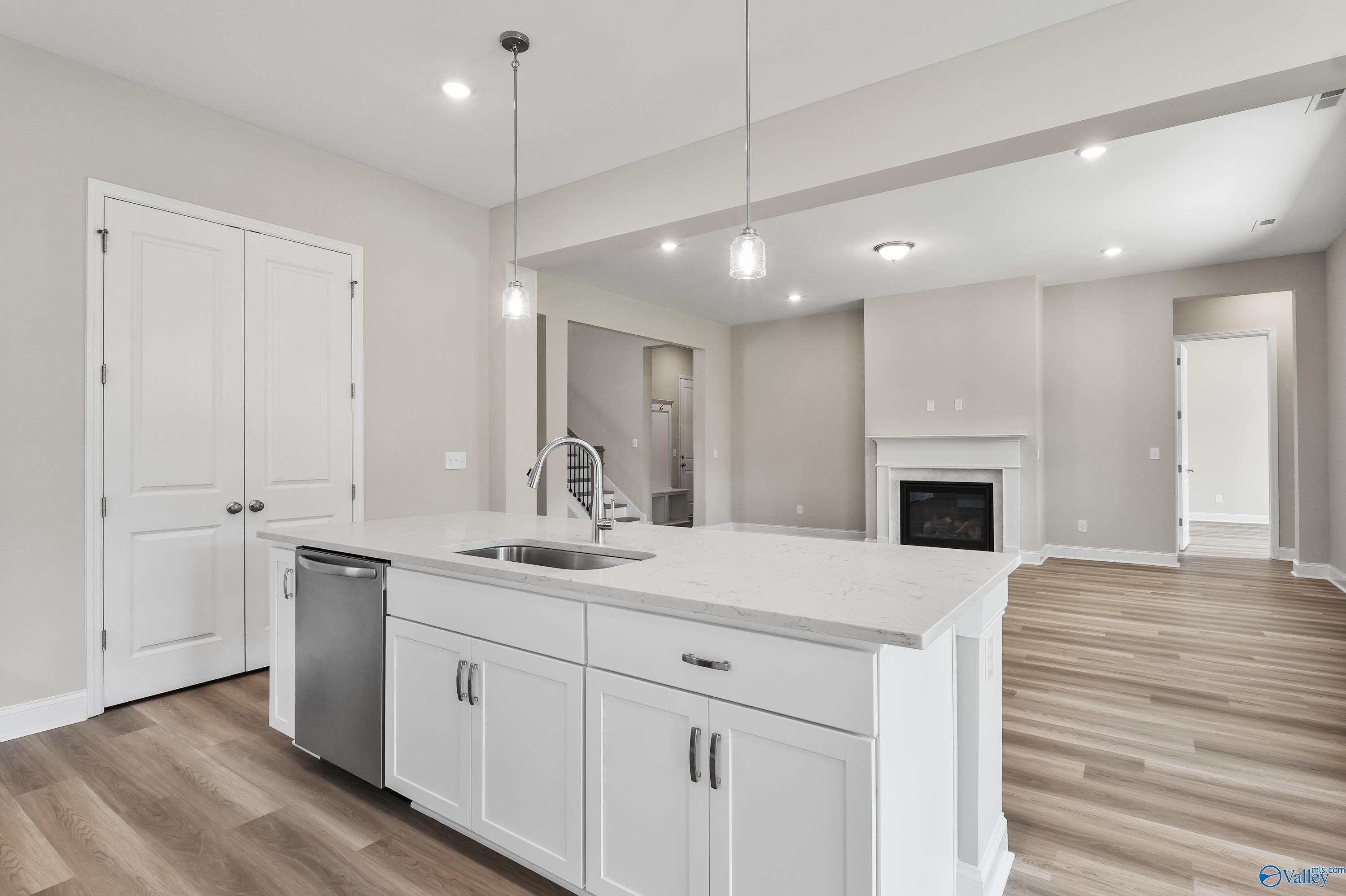 Modern white kitchen island with sink, dishwasher, and open fireplace in The Haven 5-bedroom home by Evermore Homes, Owens Cross Roads, AL