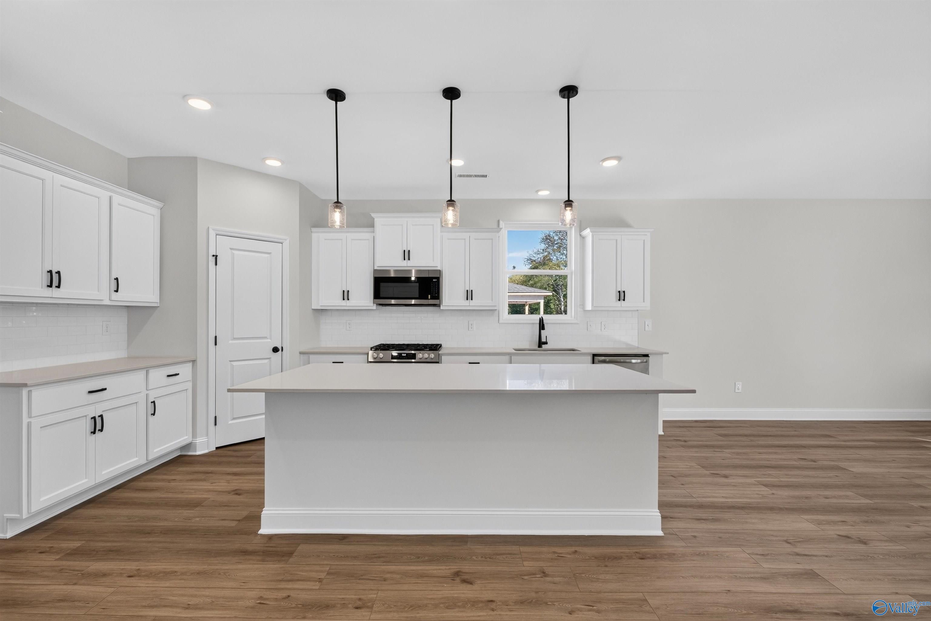 White kitchen with large island, pendant lights, and stainless appliances in Davidson Homes Ashport L plan, Berry Cove, Alabama