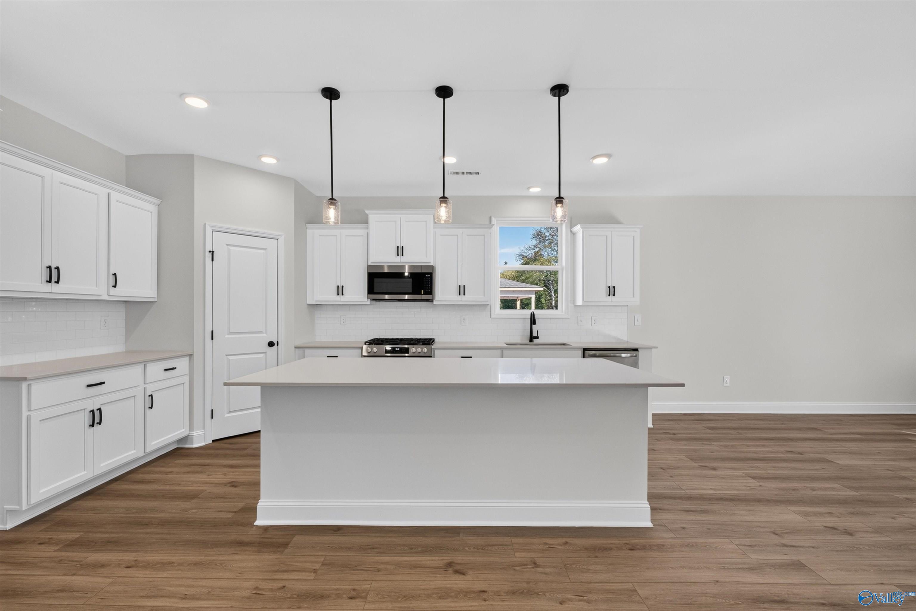 White kitchen with large island, pendant lights, and stainless appliances in Davidson Homes Ashport L plan, Berry Cove, Alabama