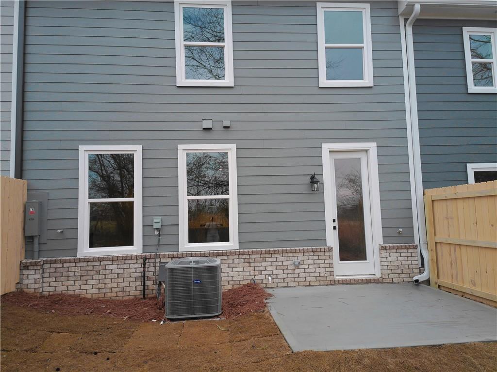 Modern gray two-story home back exterior with glass door, large windows, concrete patio, AC unit, and wooden fence in Lake Shore, Winder, Georgia