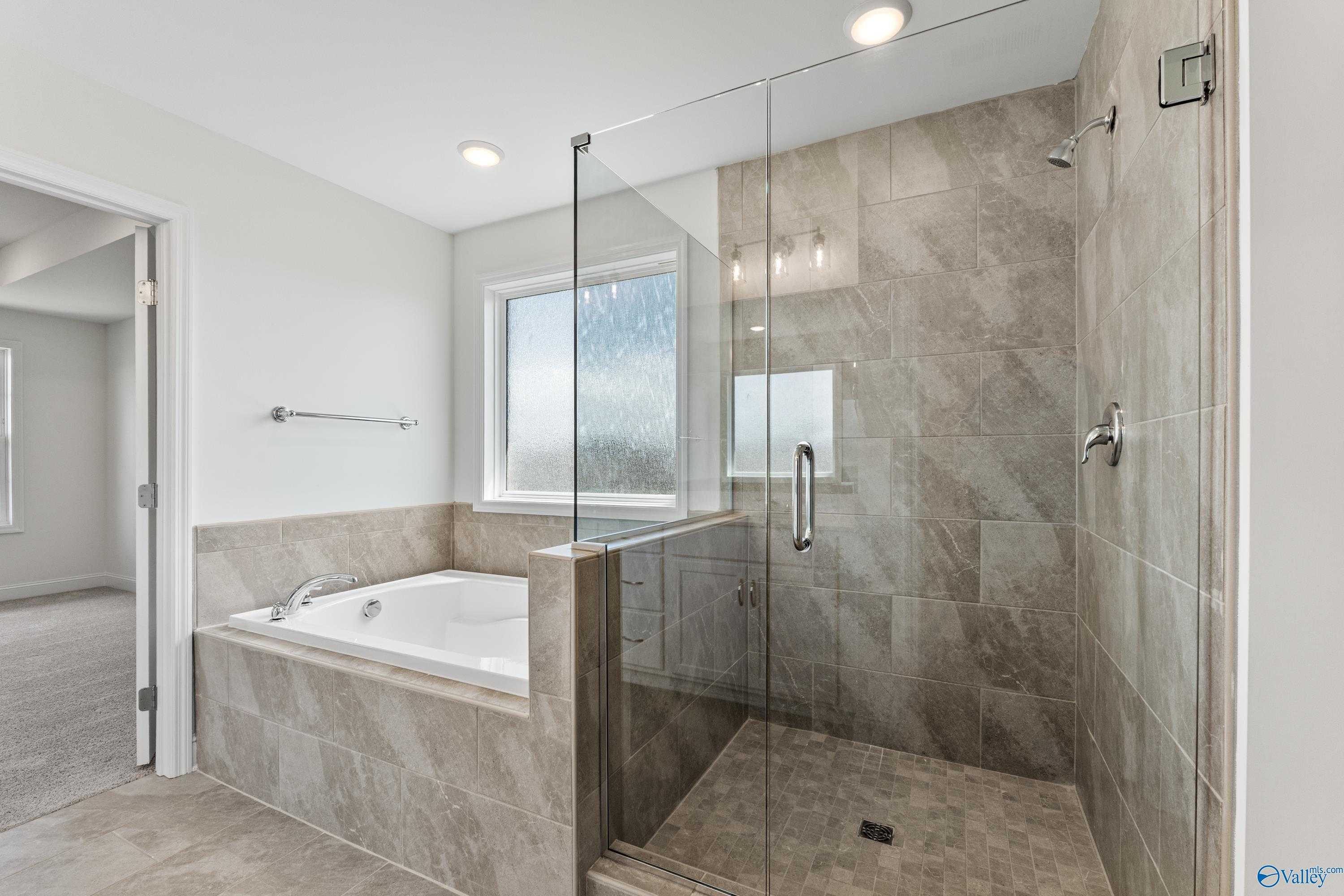 Modern master bathroom featuring glass shower, freestanding tub, and gray tile in Davidson Homes The Madison B, Meridianville, AL