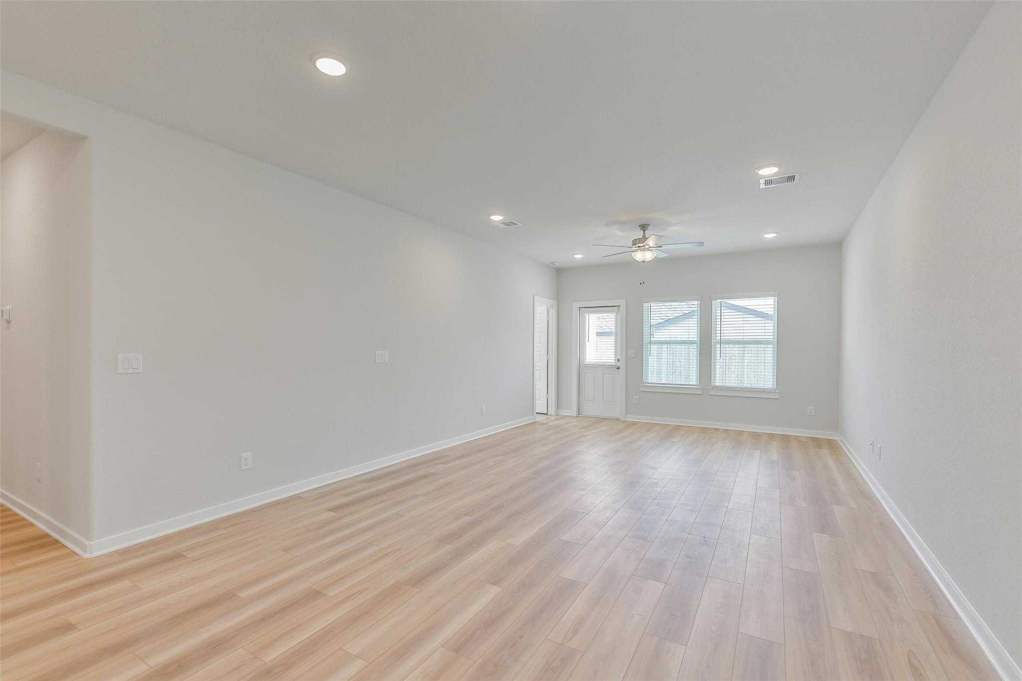 Spacious empty living room with light hardwood floors, ceiling fan, recessed lights, and large windows in Davidson Homes The Rio Grande H, Magnolia TX