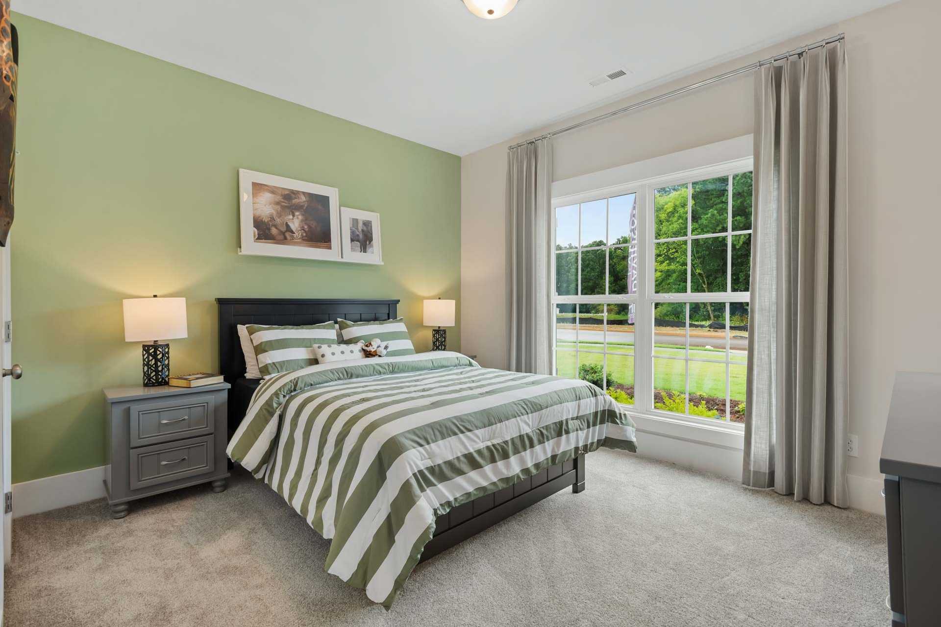 Cozy bedroom at Durham Farms in Harvest Alabama with green accent wall, striped bedding, nightstands, and large window view