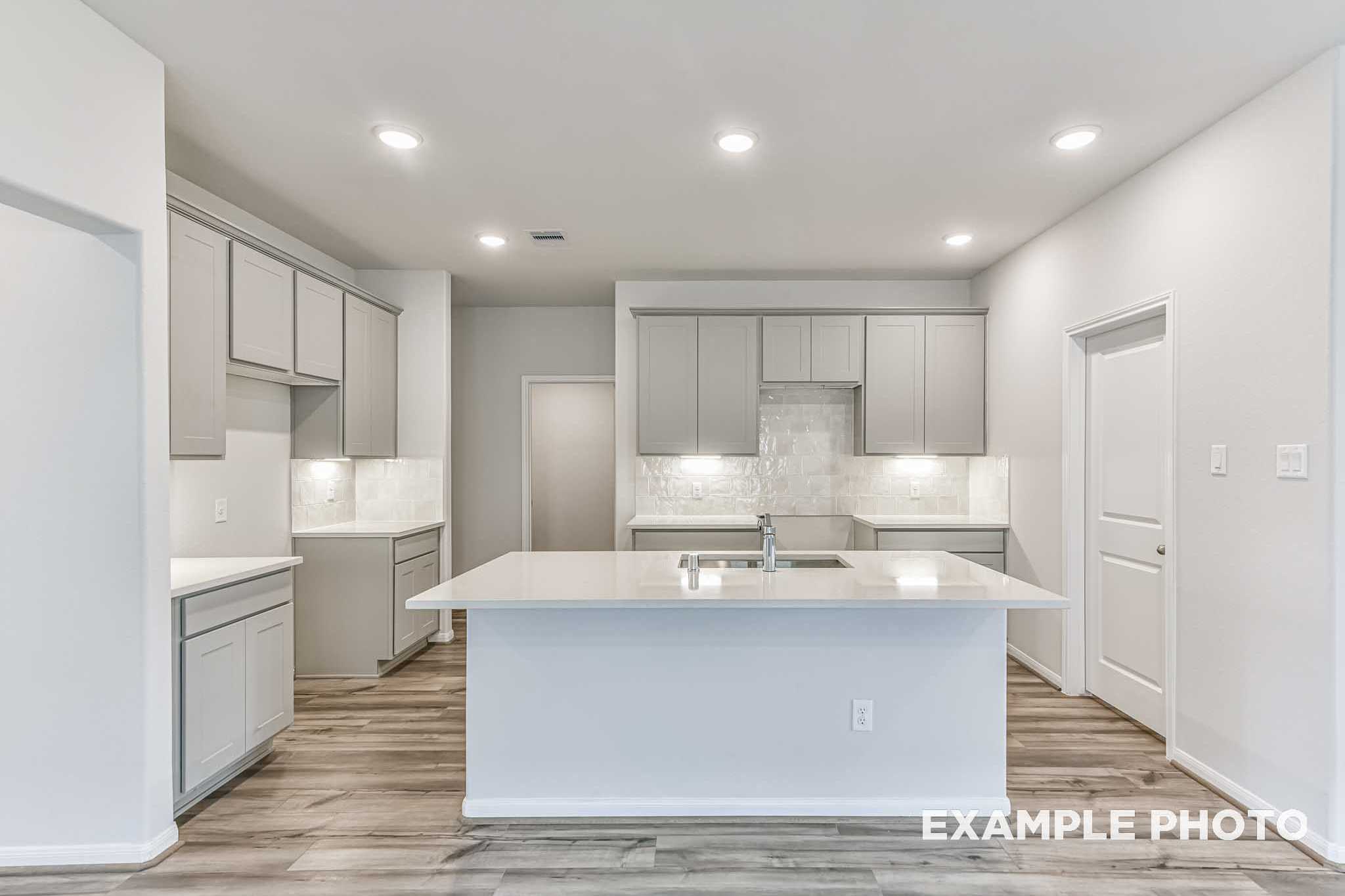 Spacious modern kitchen in The Laguna A with white cabinets, quartz island sink, subway tile backsplash, hardwood floors