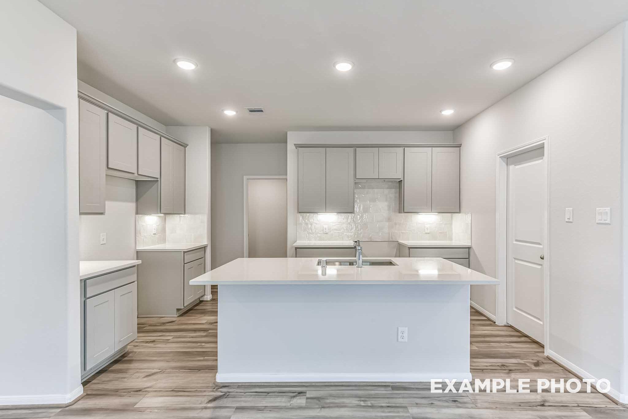 Spacious modern kitchen in The Laguna A with white cabinets, quartz island sink, subway tile backsplash, hardwood floors
