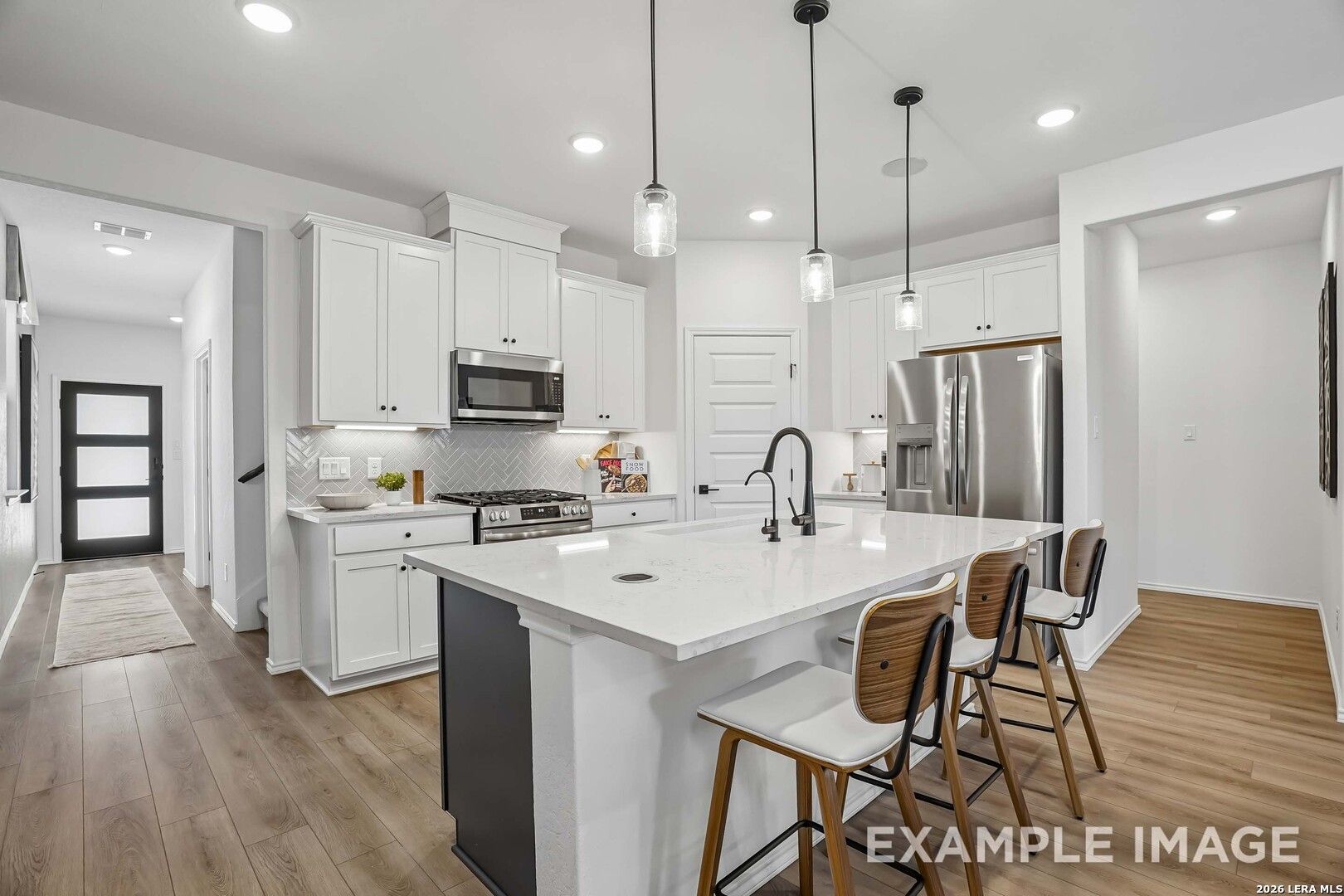 White kitchen with island, pendant lights, and stainless appliances in Davidson Homes The Pinecrest E, Fairway Crossing, Converse, TX