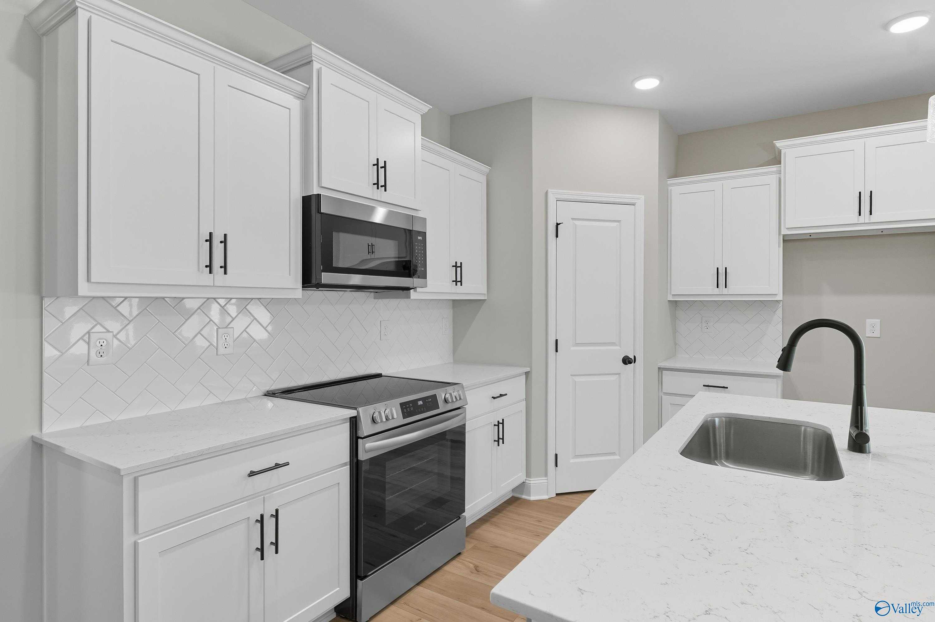 Modern kitchen with white shaker cabinets, stainless steel appliances, subway tile backsplash, and quartz island in Davidson Homes The Daphne, Meridianville, Alabama