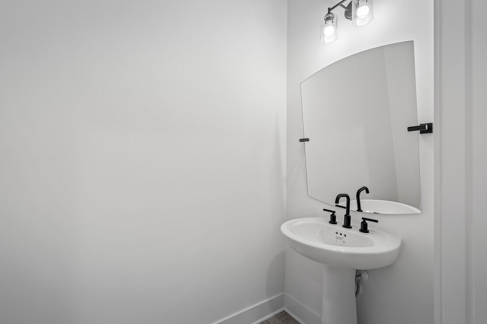 Elegant powder room with white pedestal sink, black faucet, round mirror, and sconces in Davidson Homes The Alston A, Murfreesboro, TN