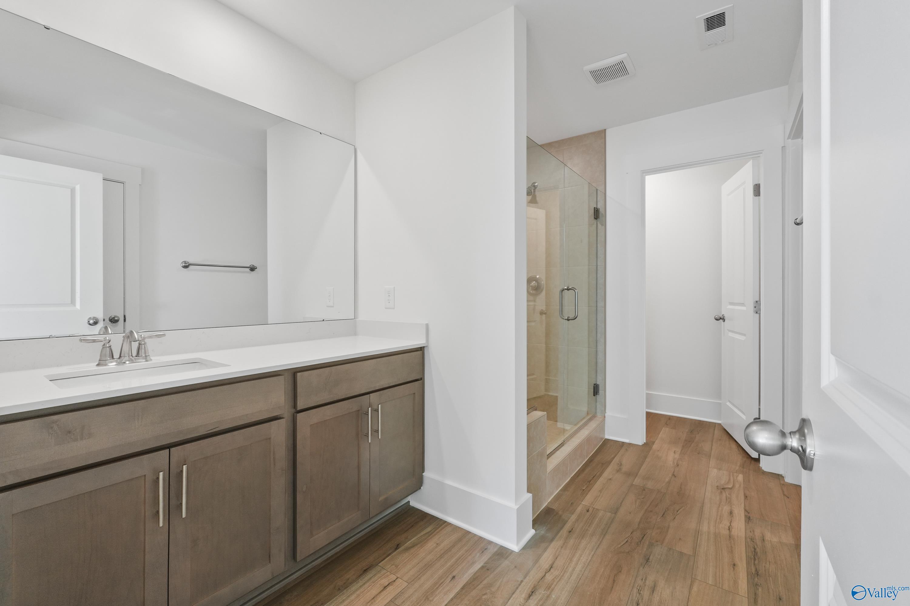Modern master bathroom featuring double gray vanity, frameless glass shower, and hardwood floors in Davidson Homes The Daphne C, Arab, Alabama