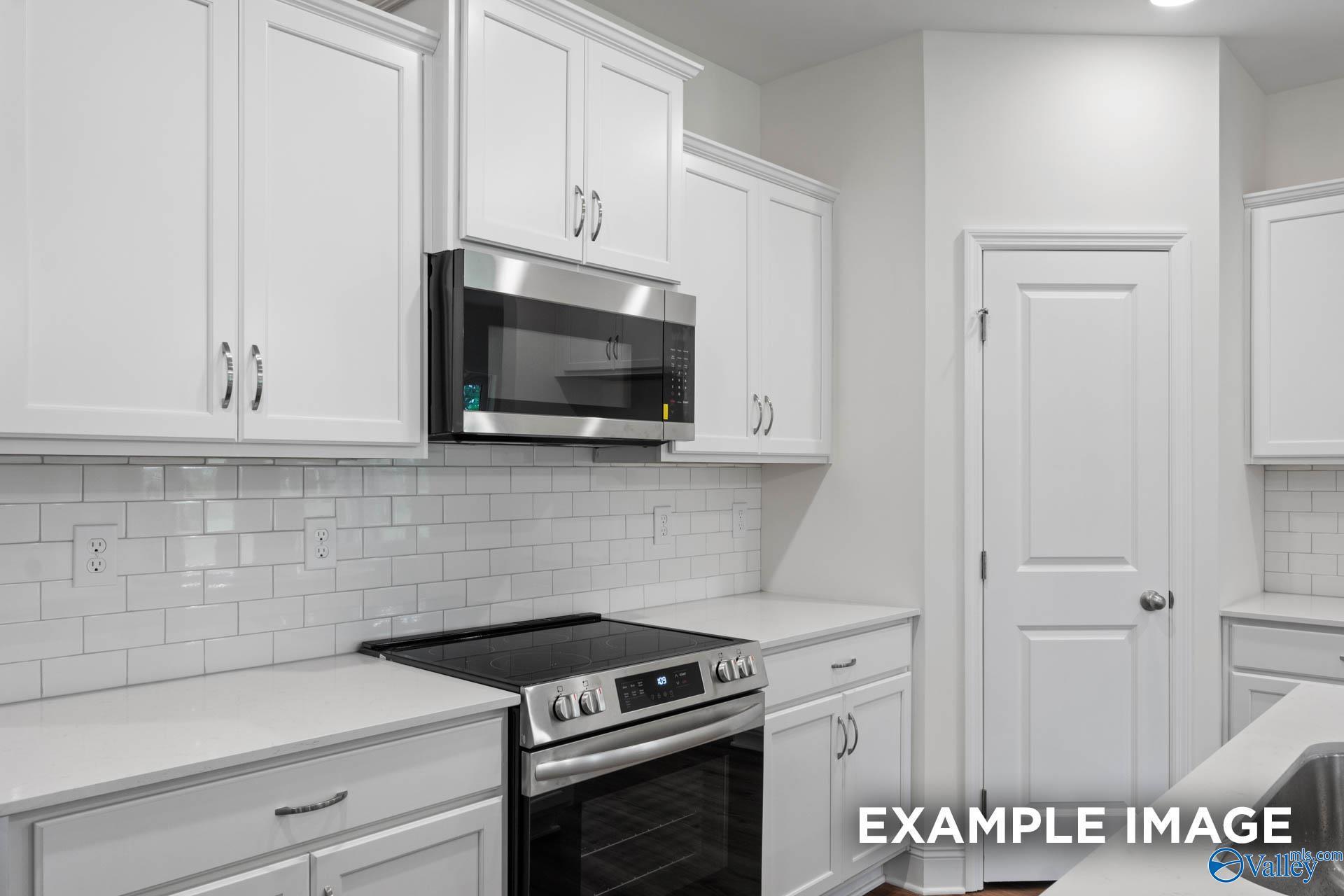 Modern white kitchen with stainless steel microwave, oven, quartz counters, subway tile backsplash in Evermore Homes Daphne E, Harvest AL