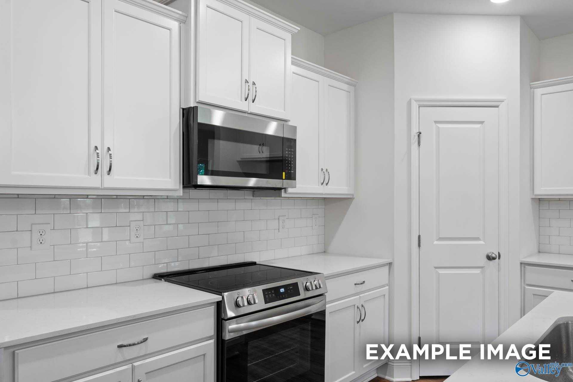 Modern white kitchen with stainless steel microwave, oven, subway tile backsplash in The Daphne D by Davidson Homes, Athens, AL