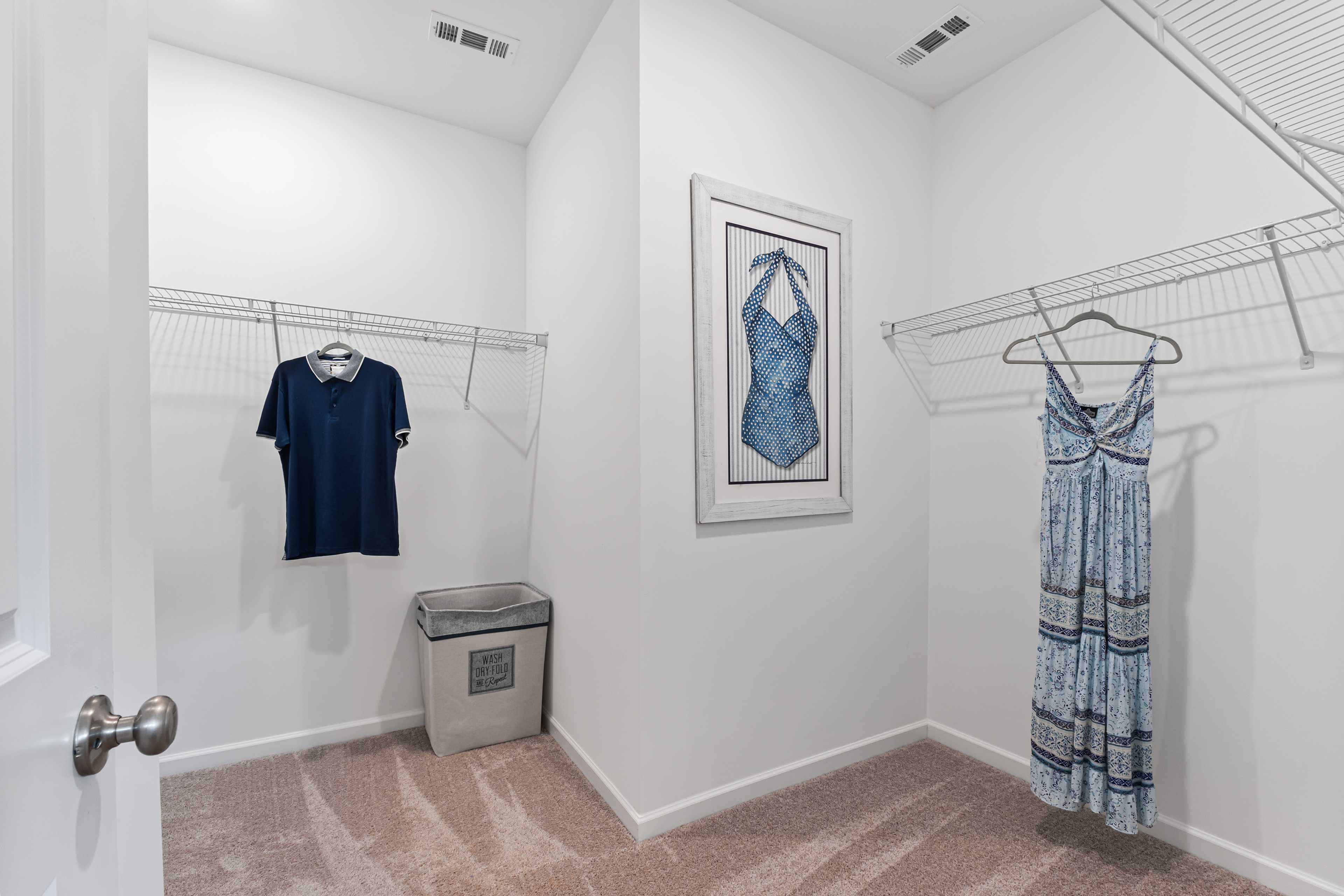 Spacious walk-in closet in Forest Glen home, Hazel Green Alabama with wire shelving, hanging clothes, and framed blue artwork