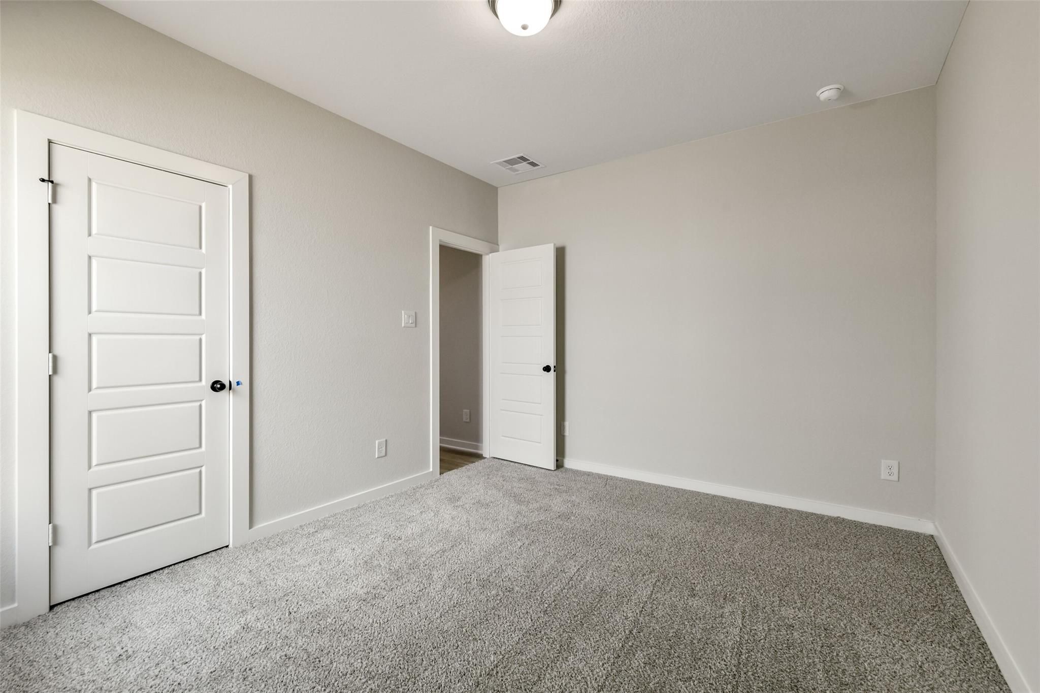 Neutral beige bedroom with white paneled doors, plush gray carpet, ceiling light in Davidson Homes The Daphne H, Crosby Texas