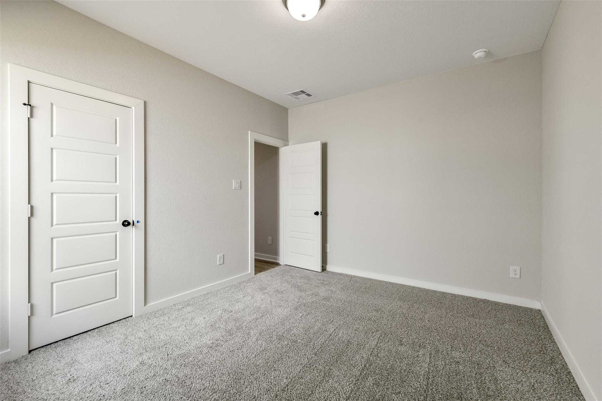 Neutral beige bedroom with white paneled doors, plush gray carpet, ceiling light in Davidson Homes The Daphne H, Crosby Texas