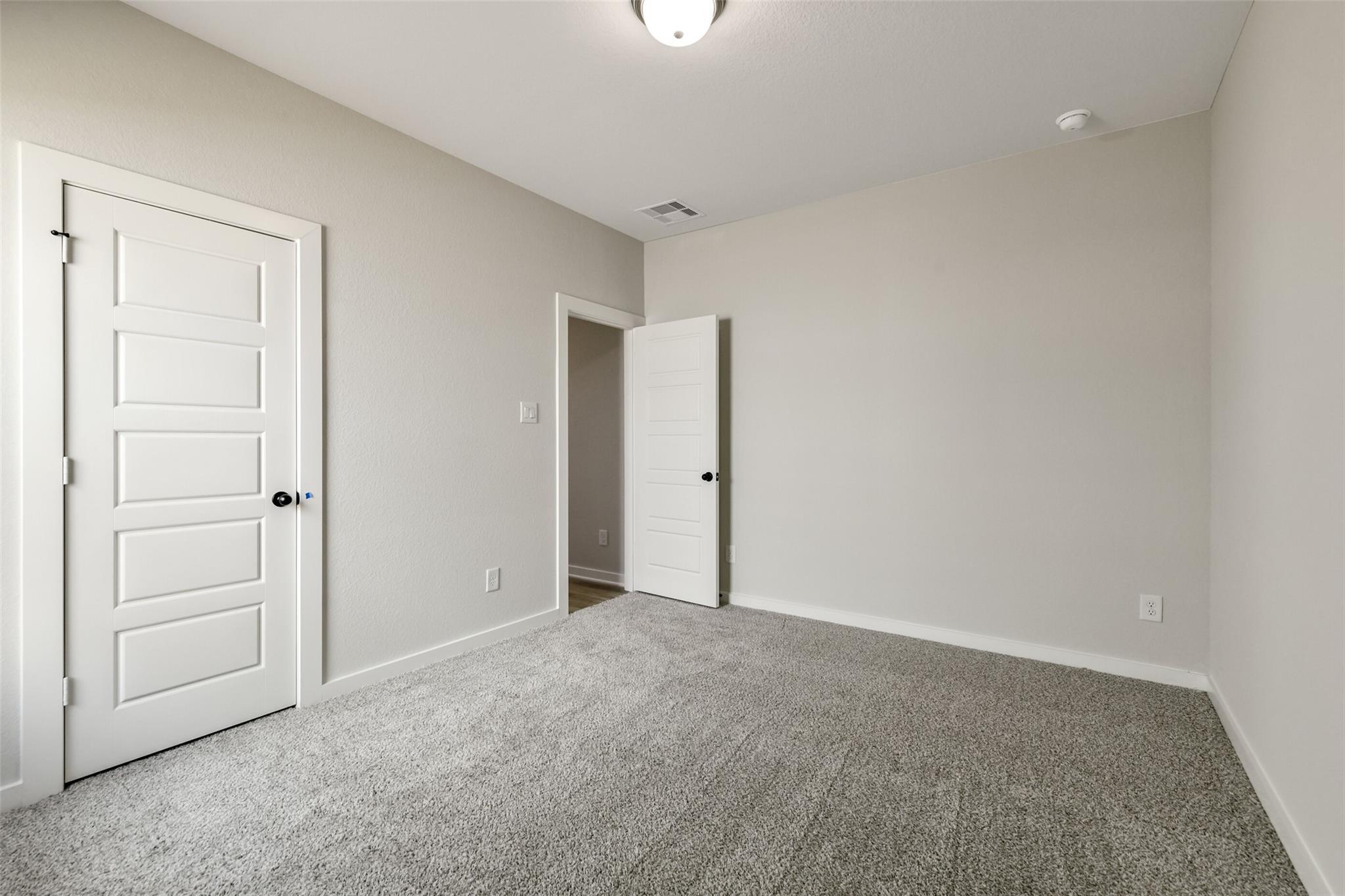 Neutral beige bedroom with white paneled doors, plush gray carpet, ceiling light in Davidson Homes The Daphne H, Crosby Texas