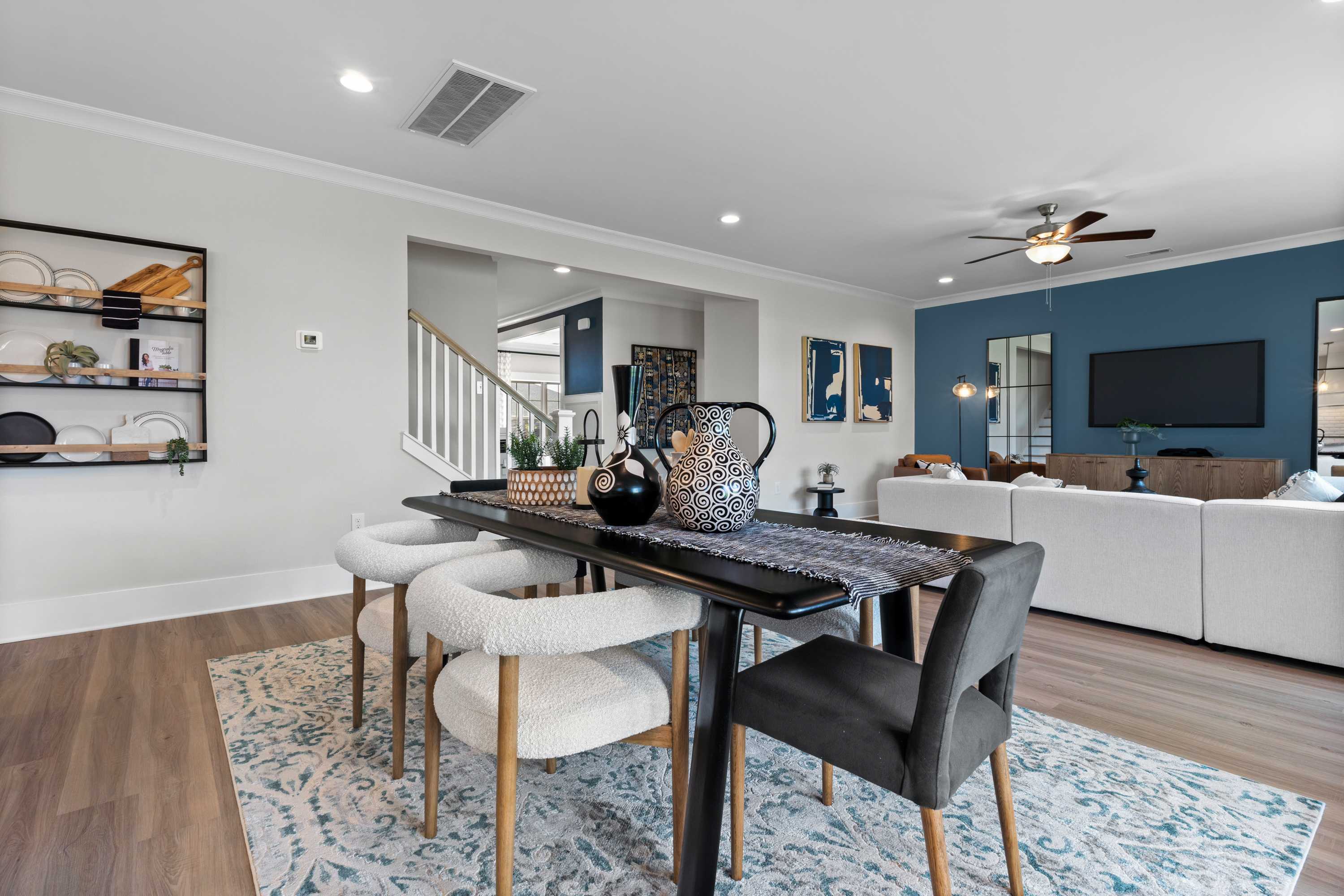 Spacious dining room in The Chelsea B home design with wooden table, upholstered chairs, blue accent wall, and open living area