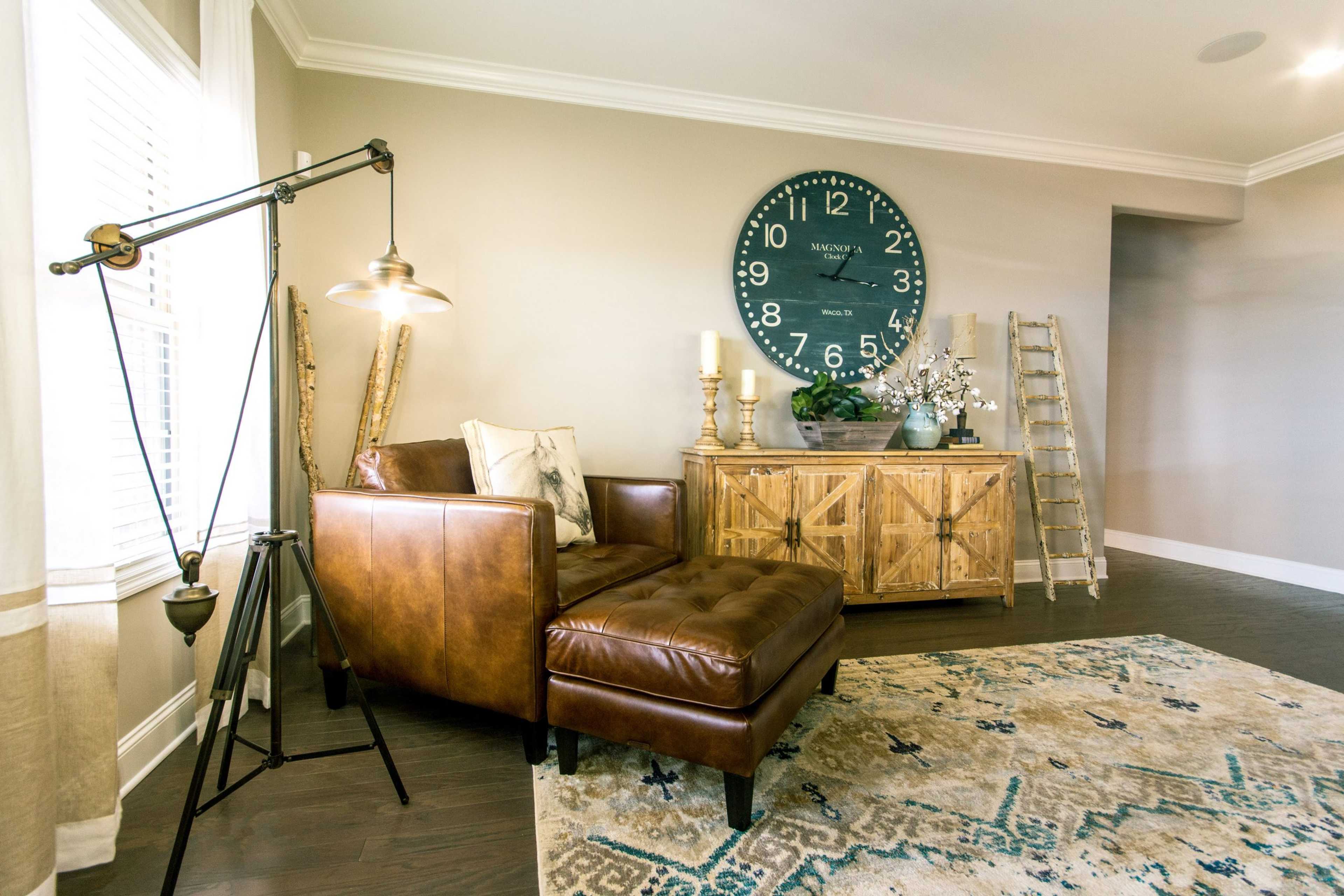 Cozy leather armchair and ottoman in Bakers Farm home, Priceville AL, with large teal wall clock, wooden credenza, and industrial lamp