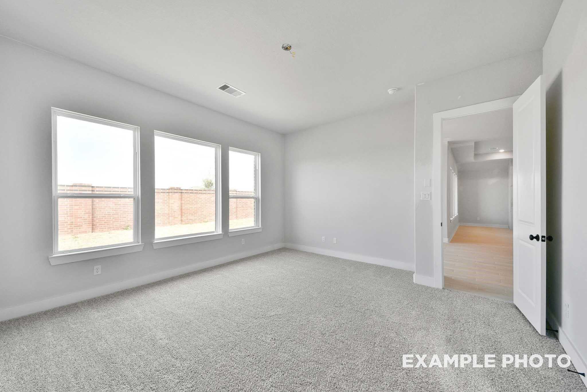 Bright empty bedroom with three large windows, gray carpet, white walls in Davidson Homes The George A, Lago Mar, Texas City
