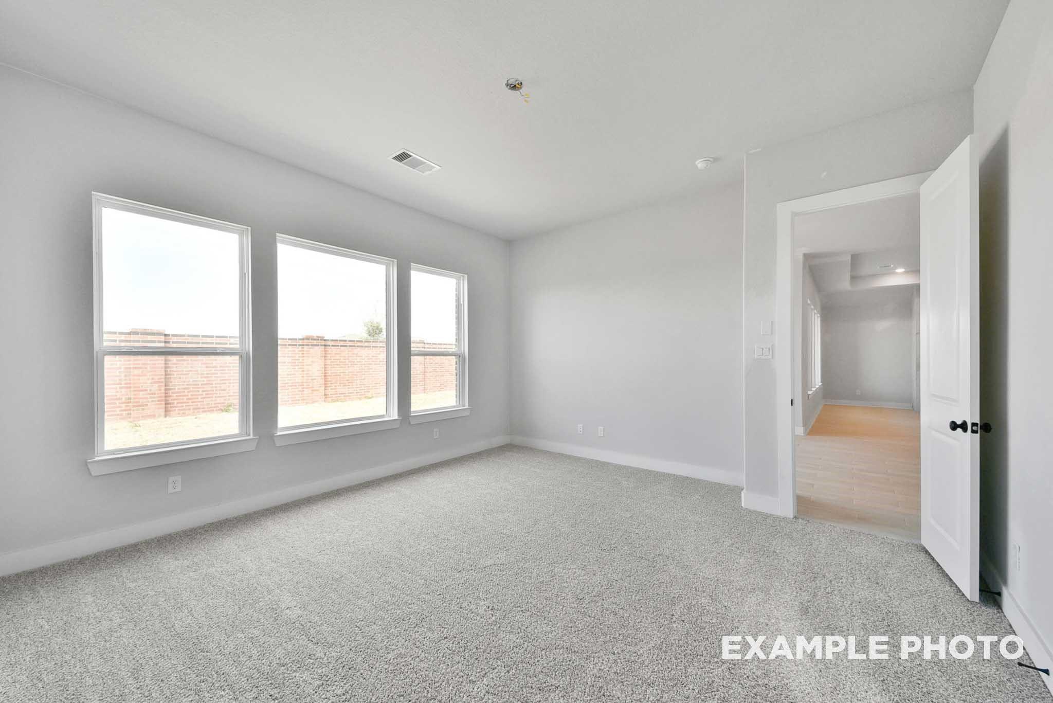 Spacious empty bedroom with large windows, gray carpet, and open hallway in Davidson Homes The George A, Lago Mar, Texas City