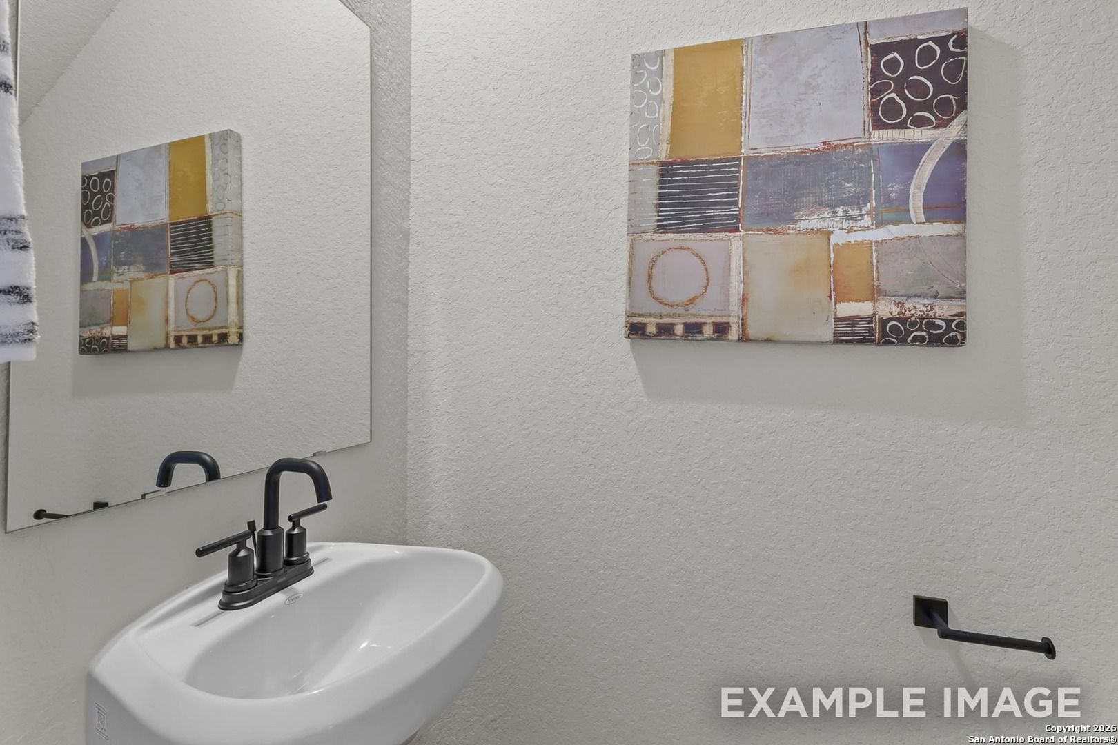 Modern powder room featuring white pedestal sink, black faucet, mirror, and abstract art in Davidson Homes The Trinity B, San Antonio
