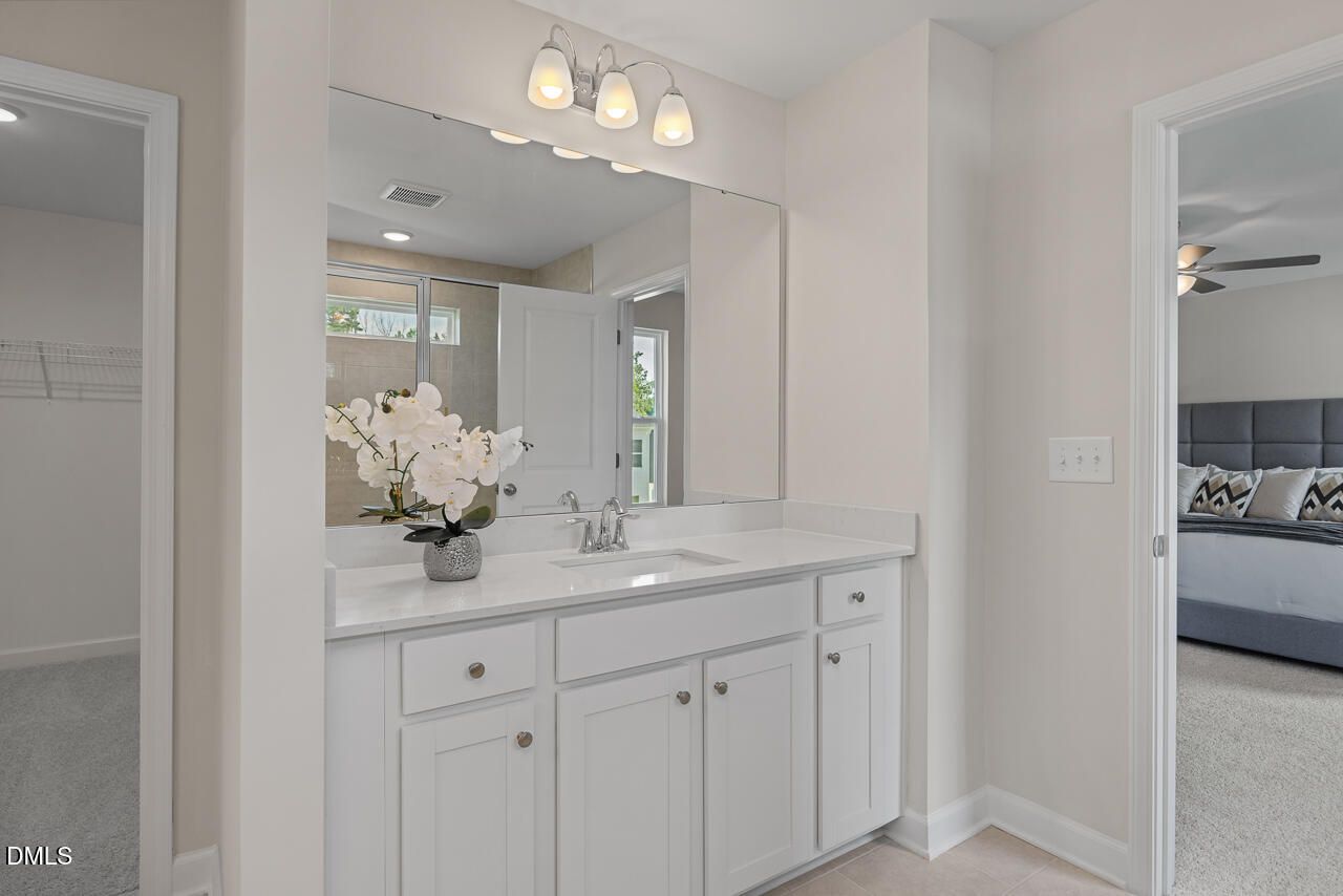 Elegant master bathroom with white double vanity, large mirror, orchids, and walk-in closet in Davidson Homes The Preston A, Lillington