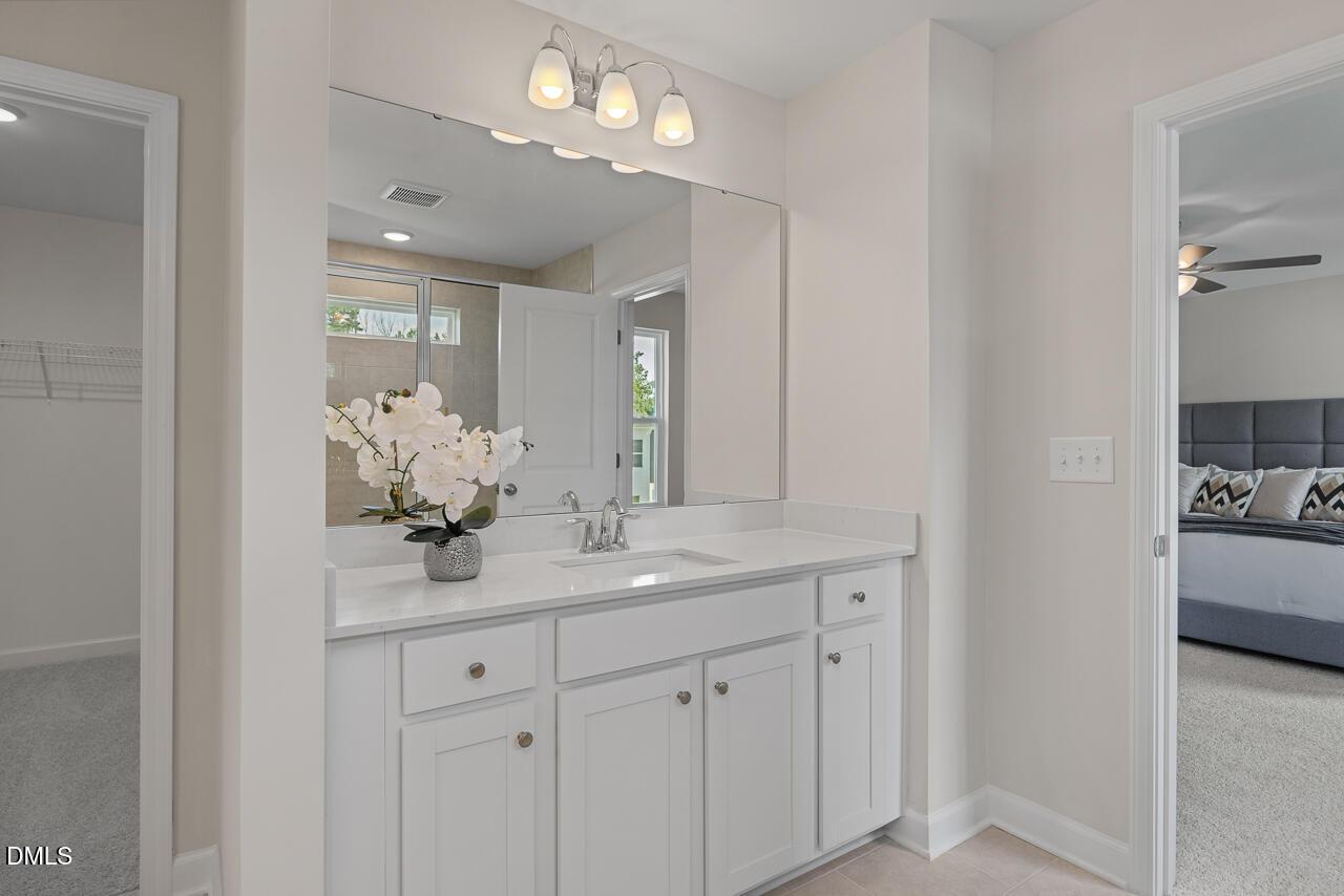 Elegant master bathroom with white double vanity, large mirror, orchids, and walk-in closet in Davidson Homes The Preston A, Lillington