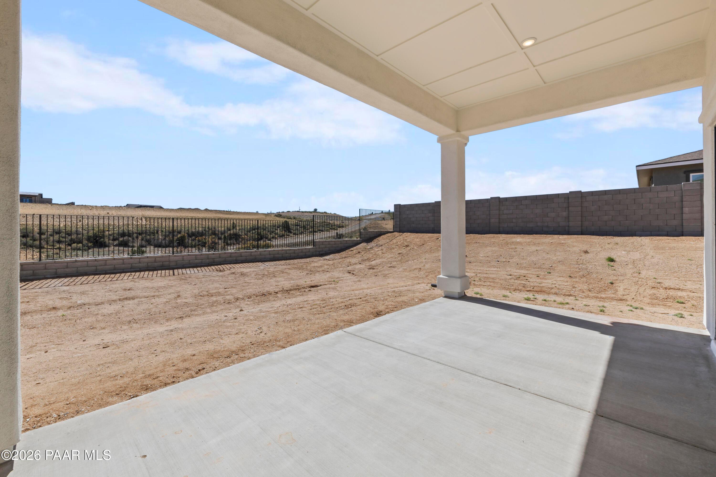 Covered back patio with white columns and concrete deck overlooking fenced desert yard in Hidden Hills, Prescott, Arizona