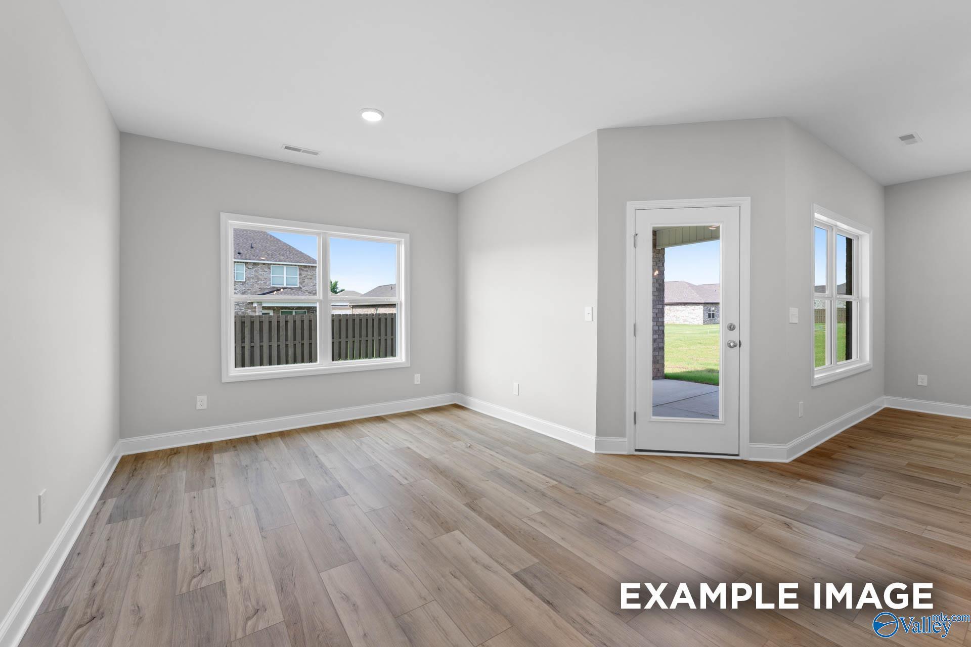 Bright family room with hardwood floors, large windows, and sliding glass door to lush backyard in The Everett B, Hazel Green, Alabama