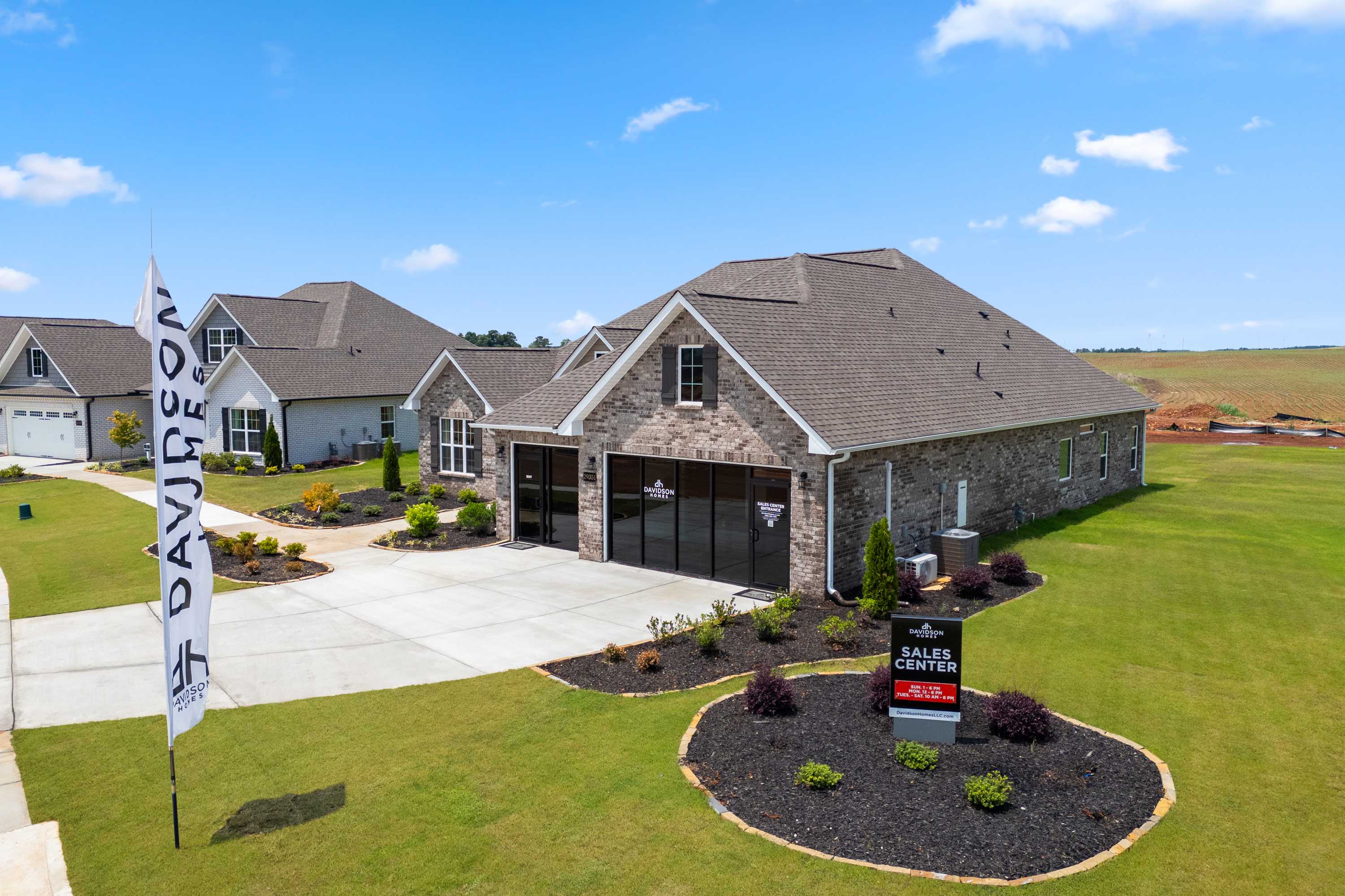 Davidson Homes sales office at Creekside in Harvest Alabama featuring brick model home, flags, and landscaped lawn