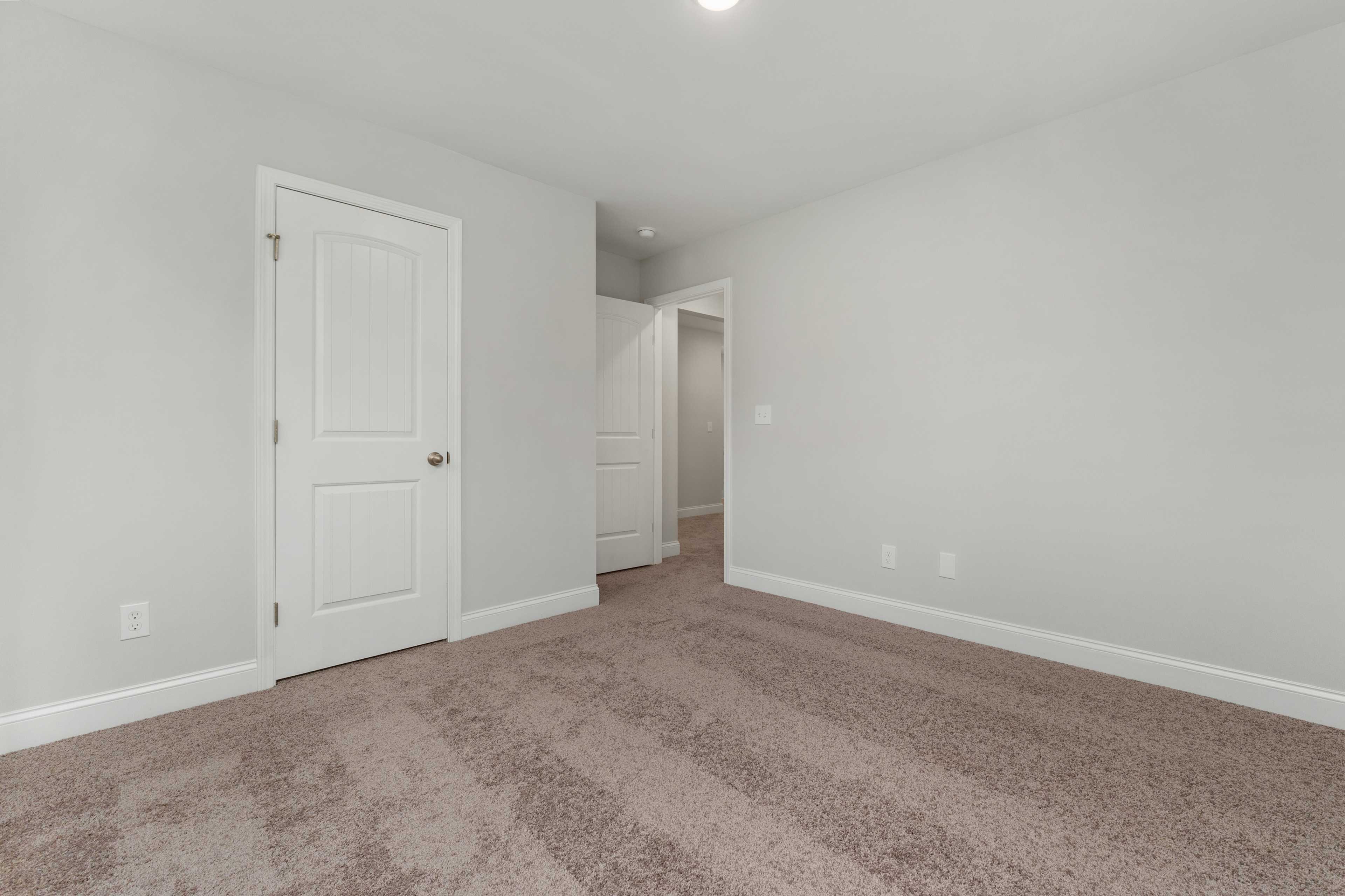 Spacious empty bedroom at Collins Lane in Meridianville, Alabama with light gray walls, white doors and beige carpet