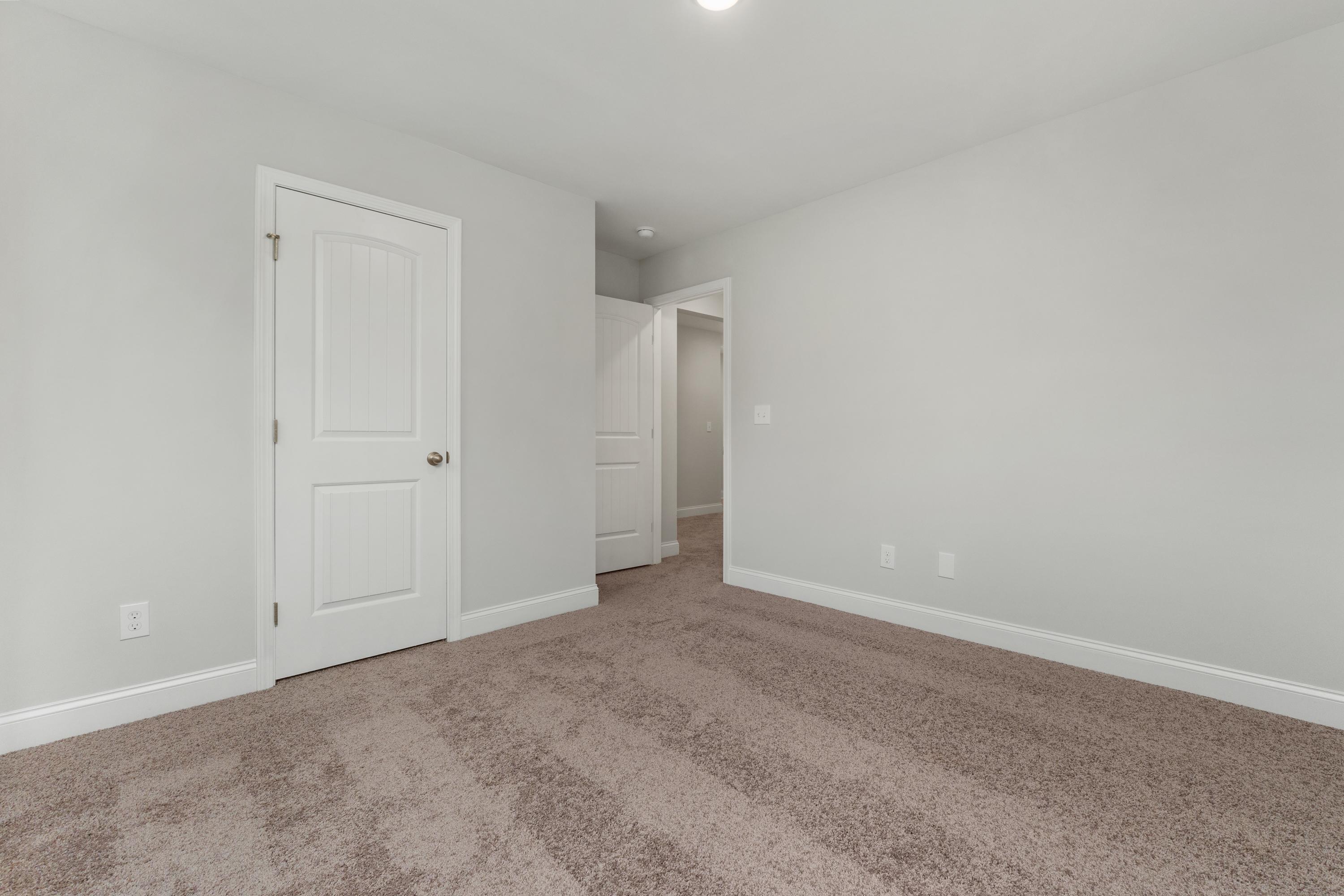 Spacious empty bedroom at Collins Lane in Meridianville, Alabama with light gray walls, white doors and beige carpet