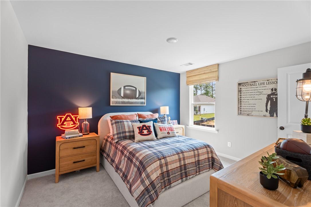 Cozy bedroom with navy accent wall, Auburn football decor, and plaid bedding in Davidson Homes The Stella B, Opelika, Alabama