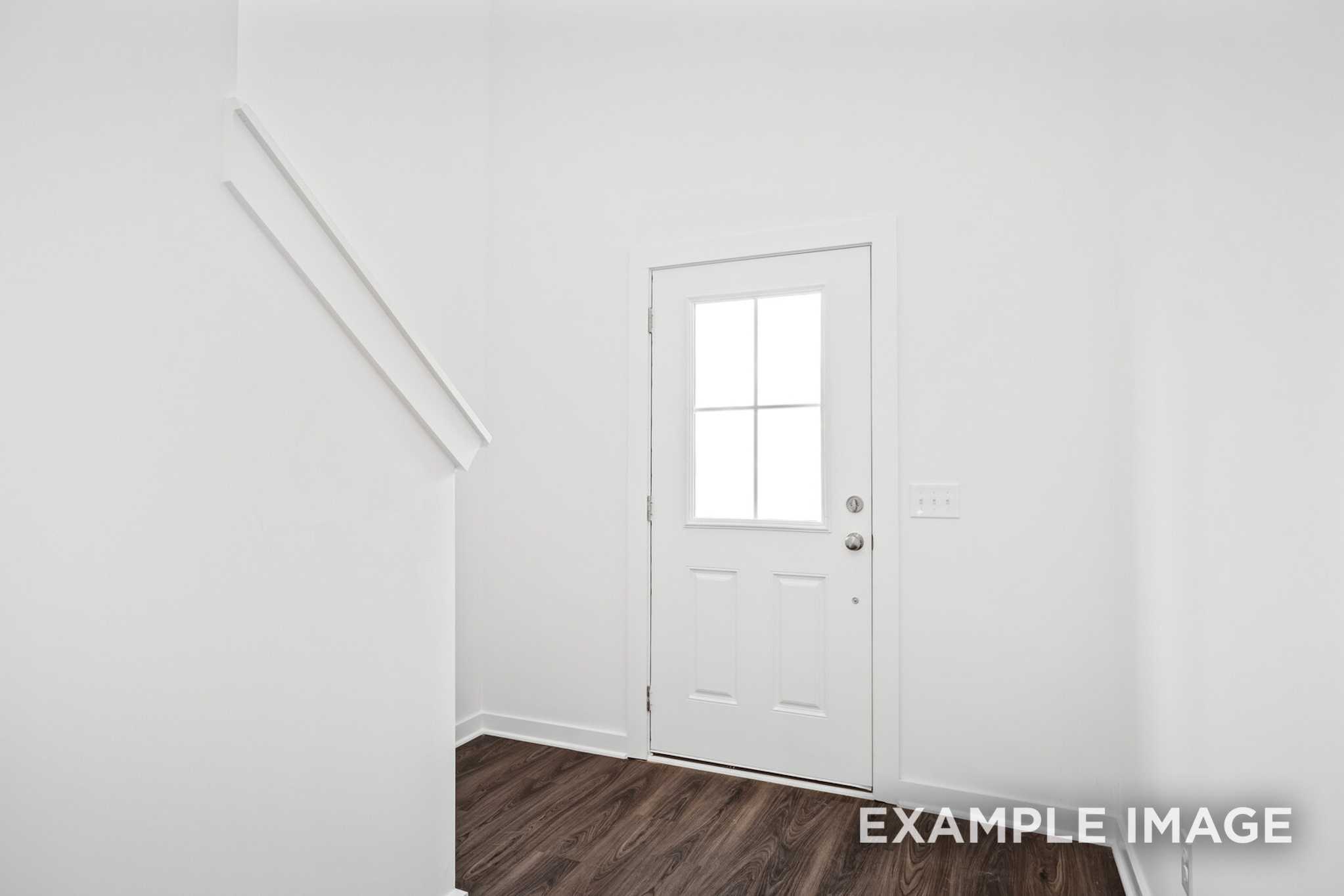 Bright white interior hallway in The Grayson C with staircase railing, paneled door, and hardwood floors