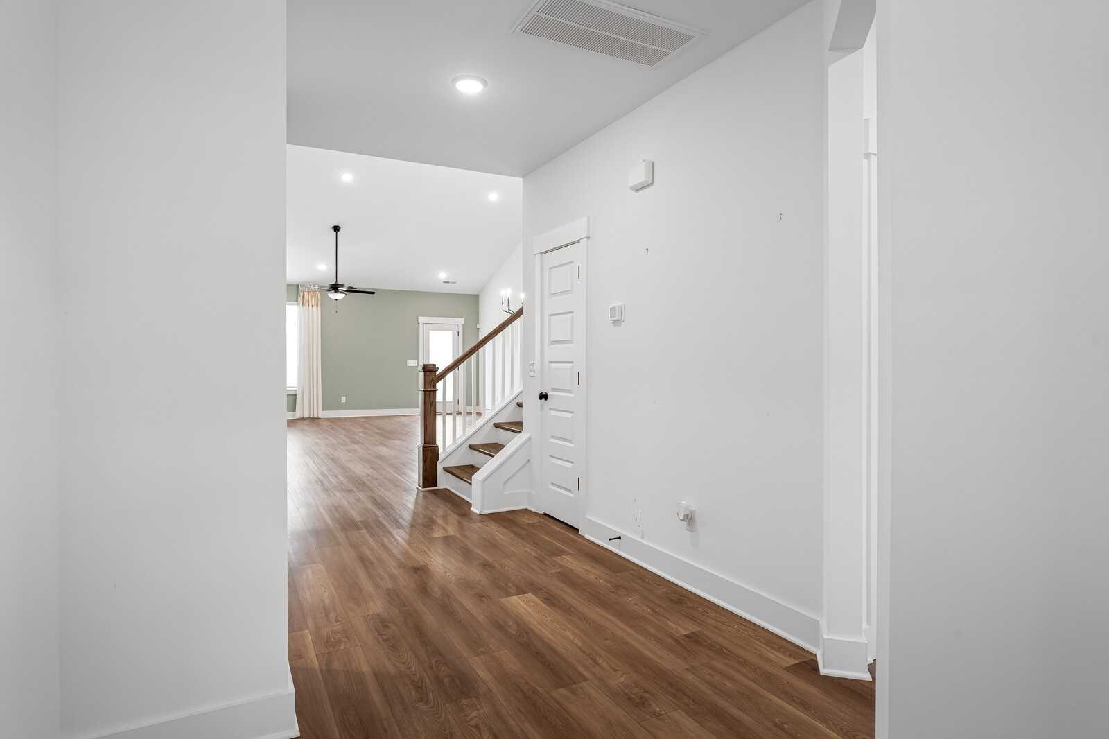 Bright entry hallway with hardwood floors, white walls, and wooden staircase in Davidson Homes The Ridgeport, Gallatin, TN