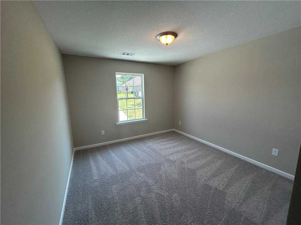 Cozy empty bedroom featuring beige walls, gray carpet, large window with lawn view, and ceiling light in Davidson Homes The Washington, Phenix City, AL