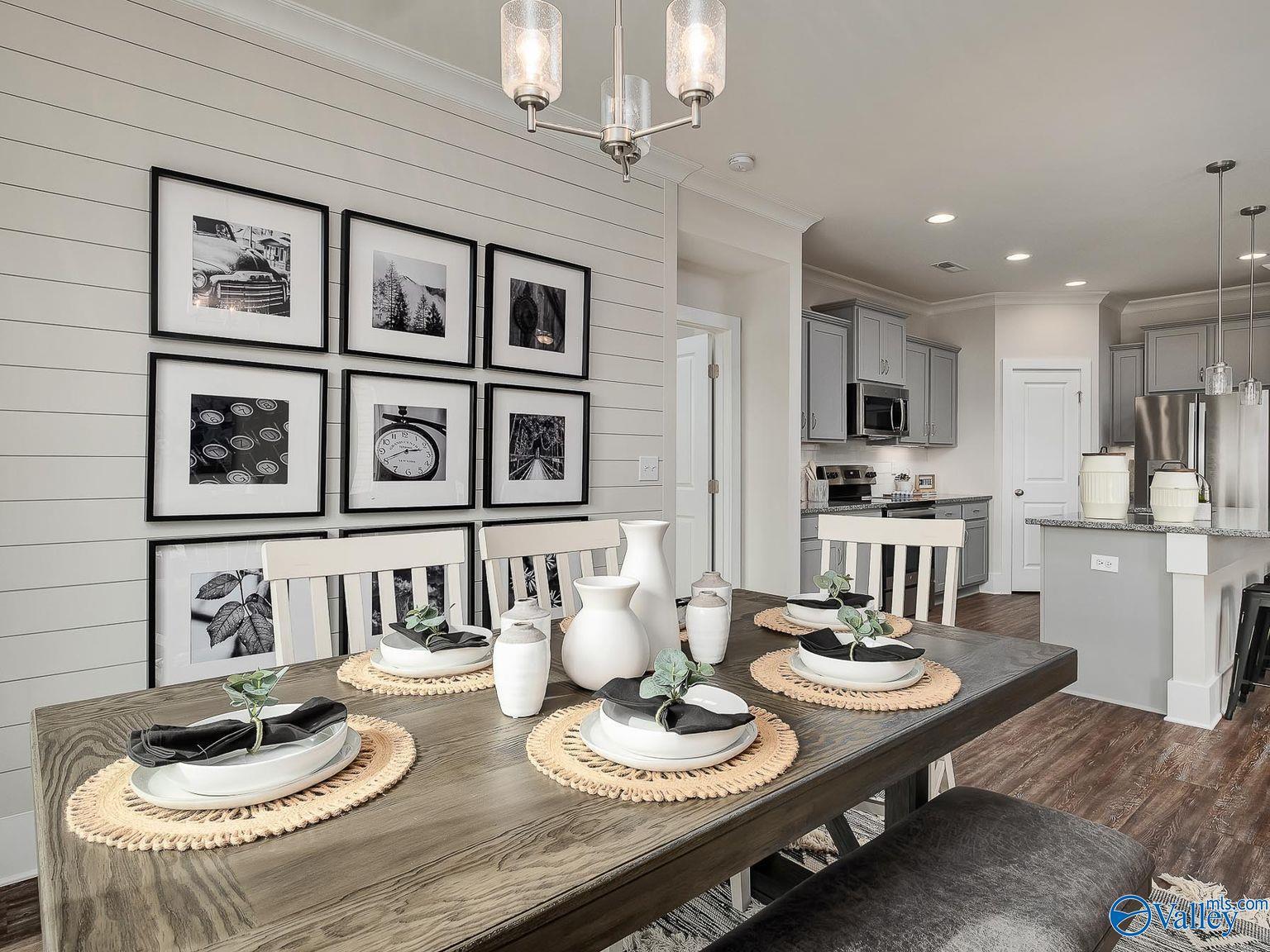 Elegant shiplap dining room with gallery wall art, set wooden table, and open kitchen island in Davidson Homes The Everett, Toney AL