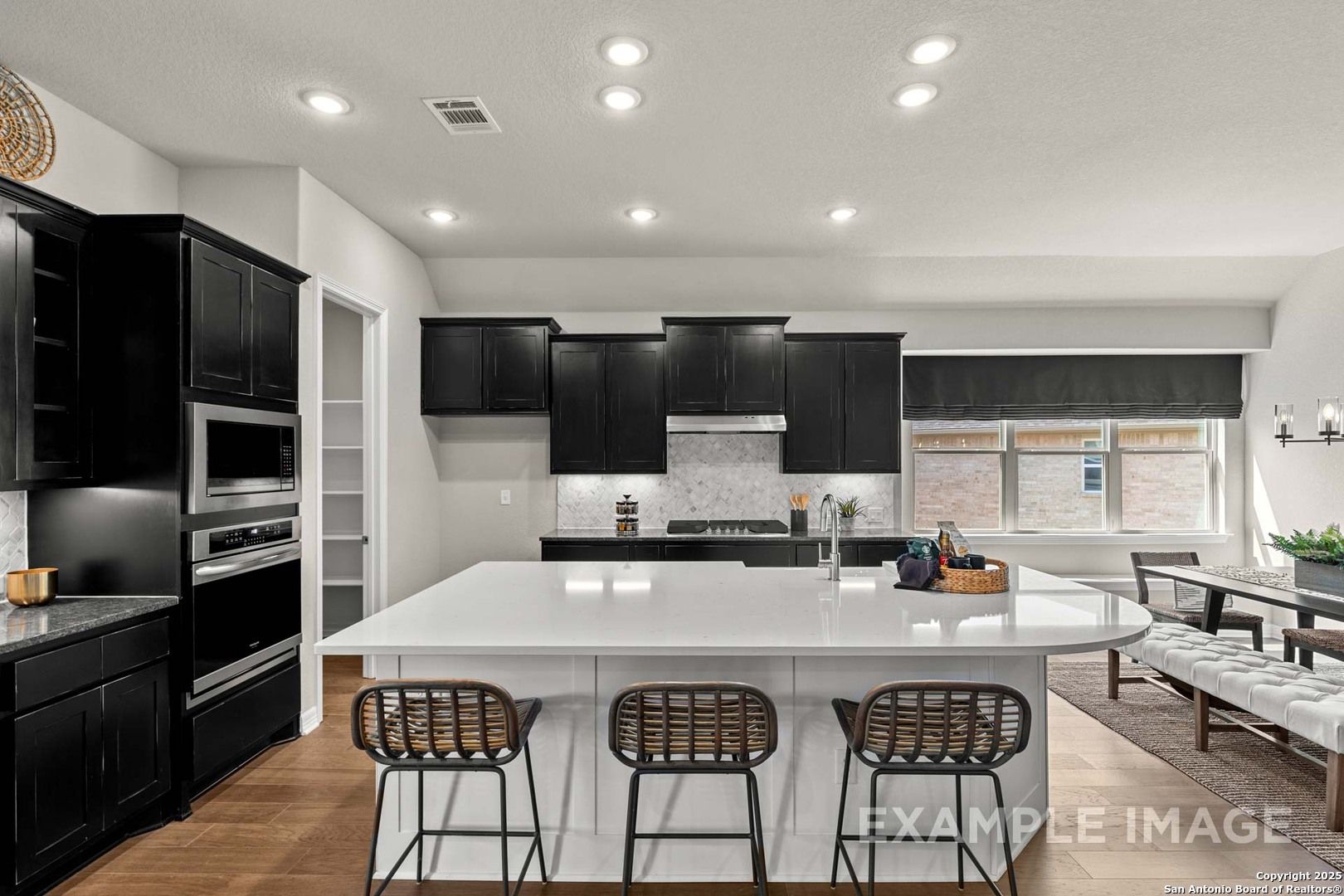 Modern kitchen featuring black cabinets, white quartz island with bar stools, and stainless appliances in Davidson Homes Summerlin B, Castroville, Texas
