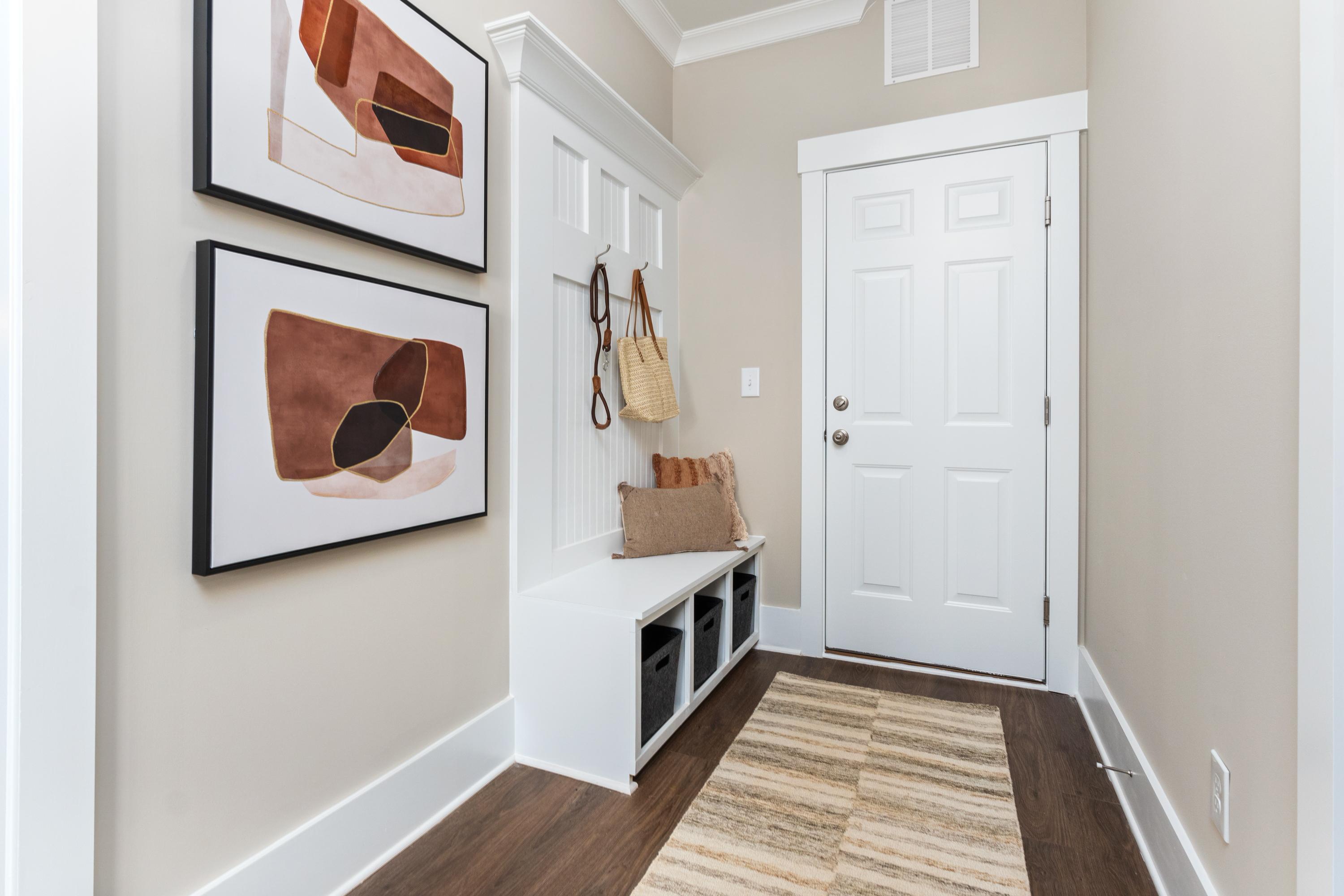 Cozy entryway in The Shelby A by Davidson Homes featuring white built-in bench, abstract wall art, coat hooks, and hardwood floors in Meridianville AL